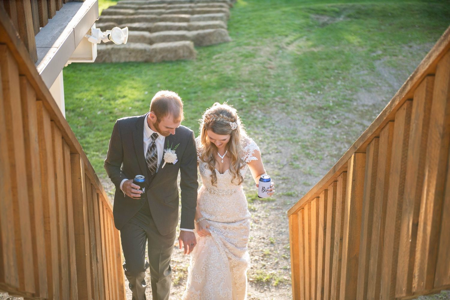 Couple walks up wooden stairs outdoors while holding drinks at rustic venue. Rum River Barn Milaca Minnesota Weddings