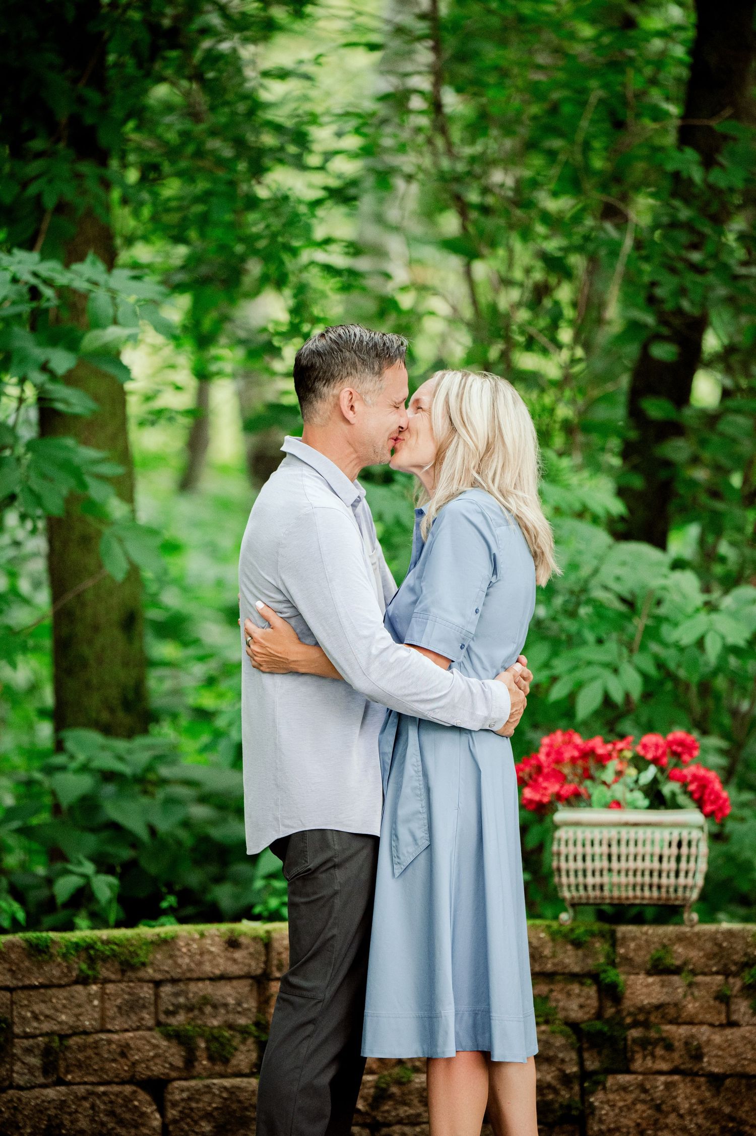 Clear Lake Family Photography: A romantic couple shares a kiss on a stone patio surrounded by lush greenery and red flowers.