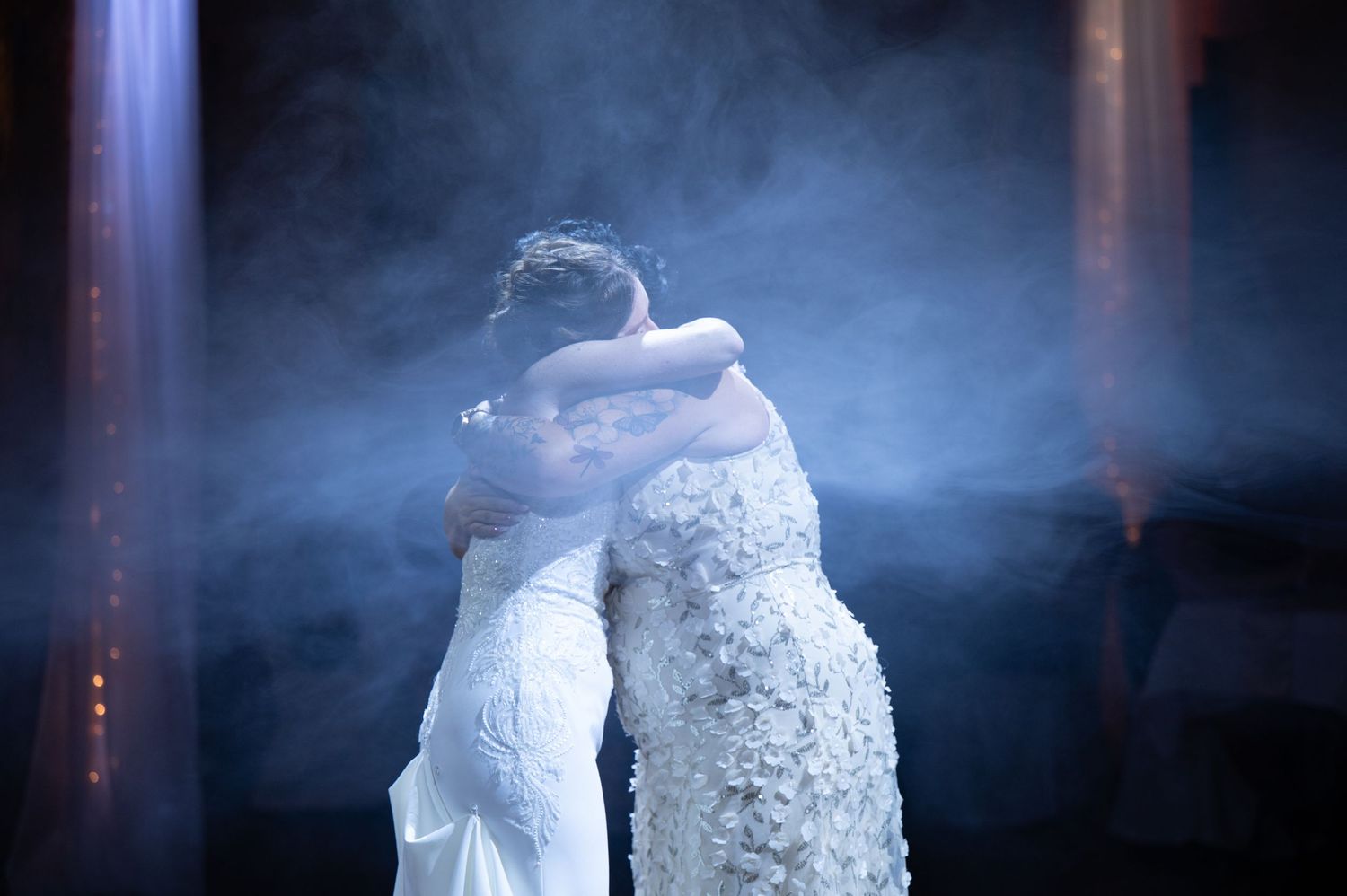 A couple embraces during their first dance surrounded by dramatic blue lighting and fog effects.