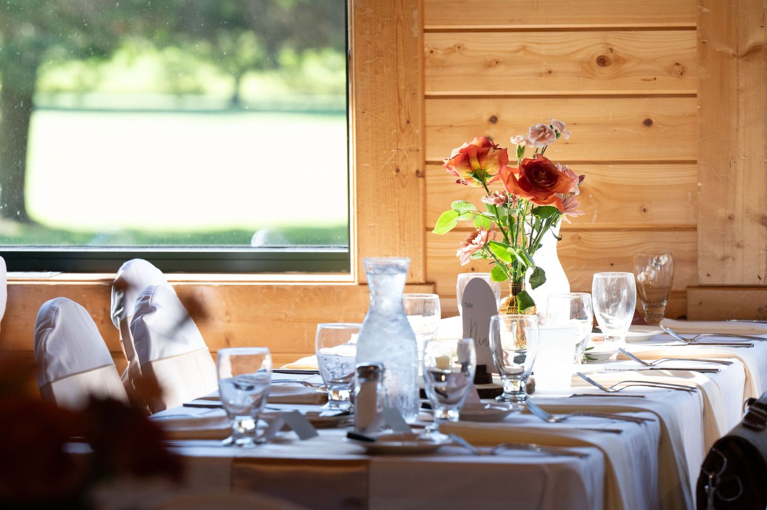 The Grands At Mulligans. An elegant table setting with white linens and bright flowers in a rustic wooden room with natural light.