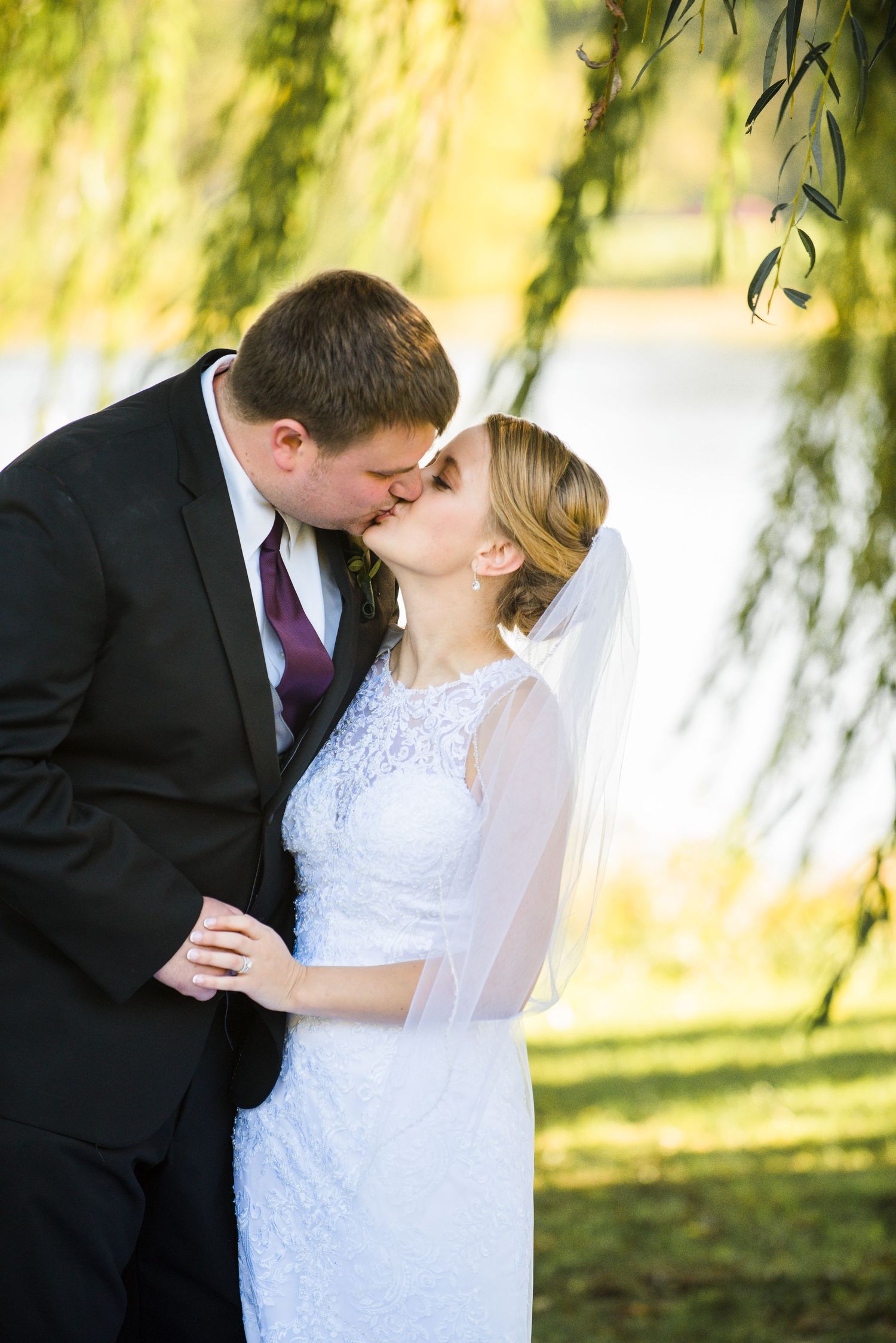 A romantic kiss between newlyweds under a weeping willow tree on their wedding day. Andover wedding at Magestic Oaks Golf Club