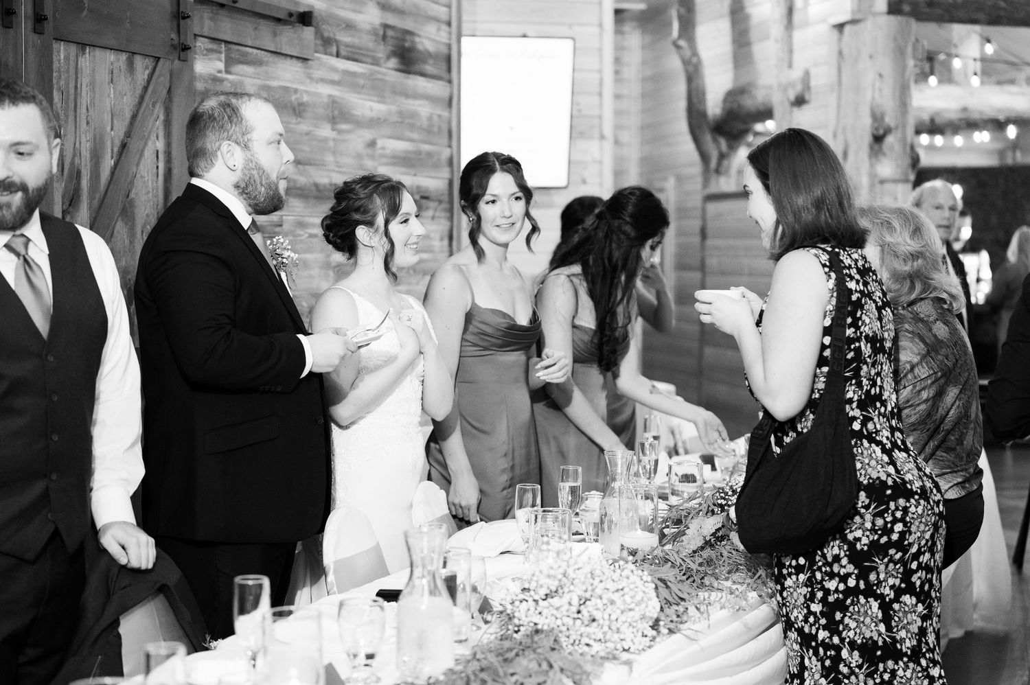 Black and white photo of wedding guests mingling at a reception in a rustic venue.