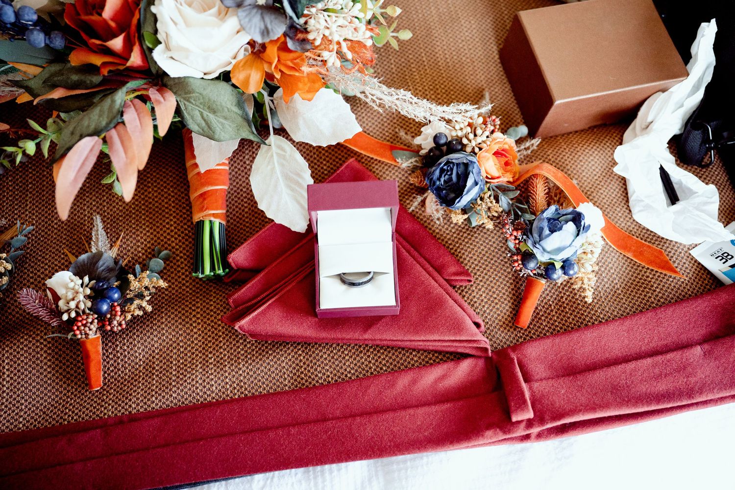 Pier B Duluth Wedding Wedding details including floral boutonnieres, ring box and burgundy decor elements on a rustic burlap surface.