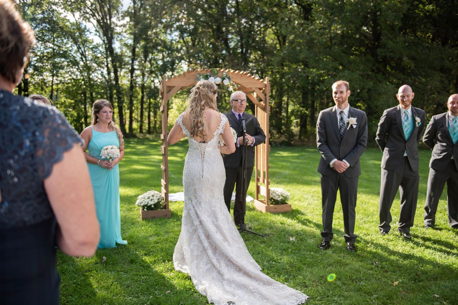 Outdoor wedding ceremony under wooden arch surrounded by trees and natural greenery. Rum River Barn Milaca Minnesota Weddings