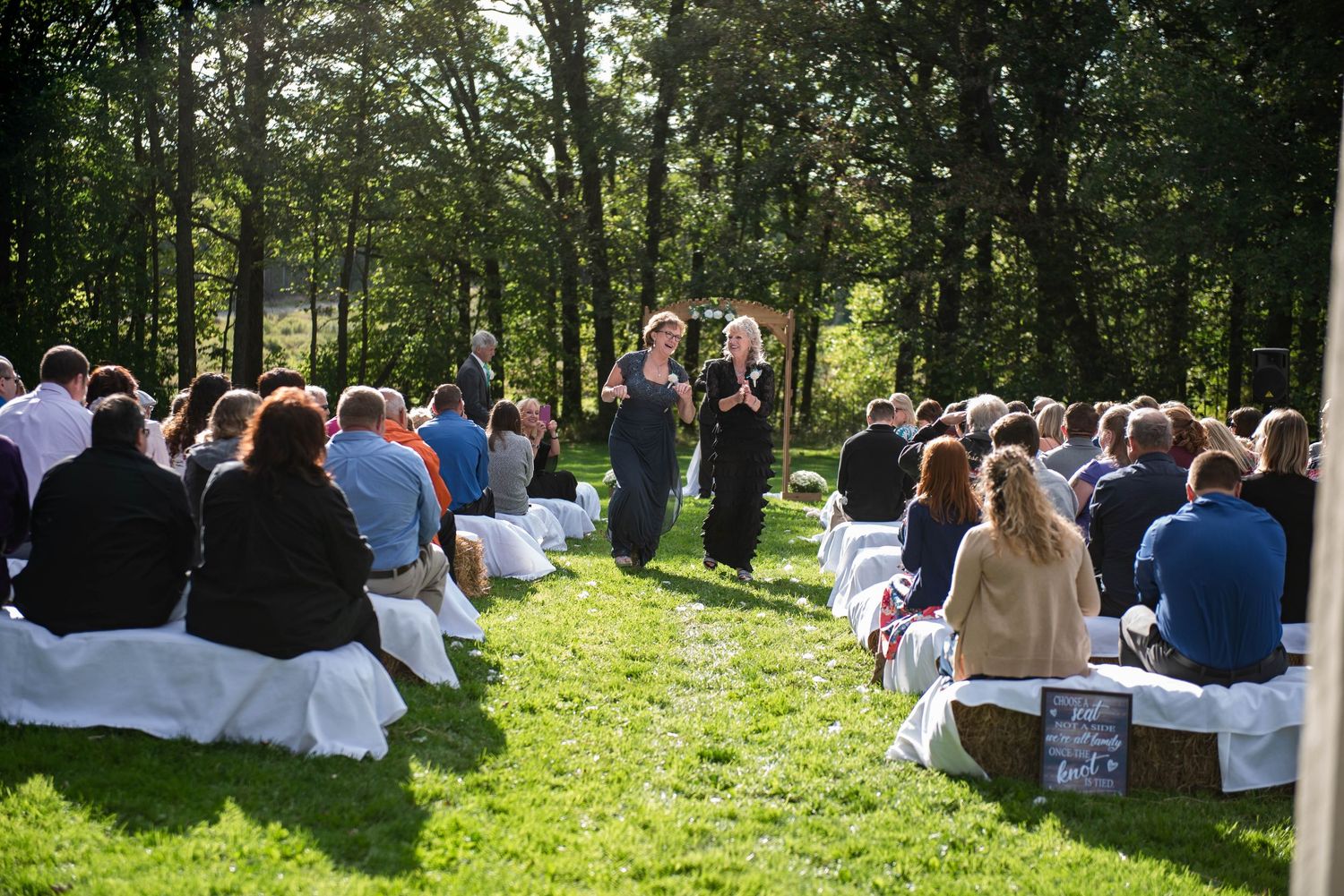 Outdoor wedding ceremony setup with white chairs on grass surrounded by tall trees. Rum River Barn Milaca Minnesota Weddings