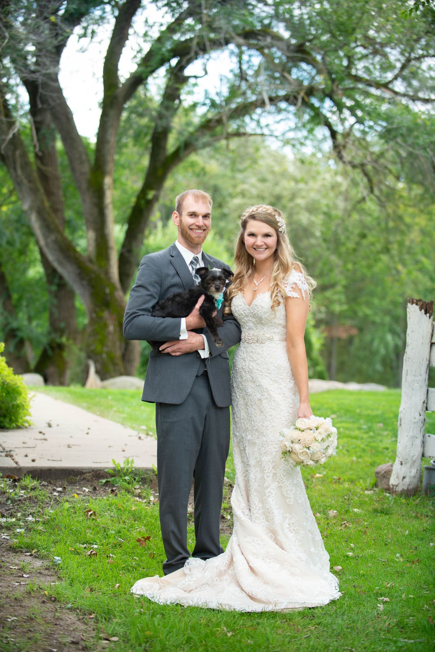 A wedding couple poses outdoors on a path with greenery and trees in the background. Rum River Barn Milaca Minnesota Weddings