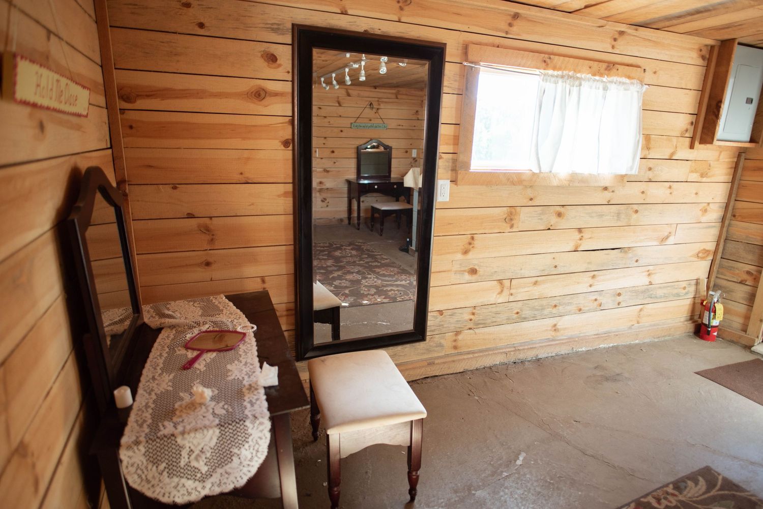 Interior view of a rustic wooden cabin with exposed beams, plank walls, and natural light streaming through windows.