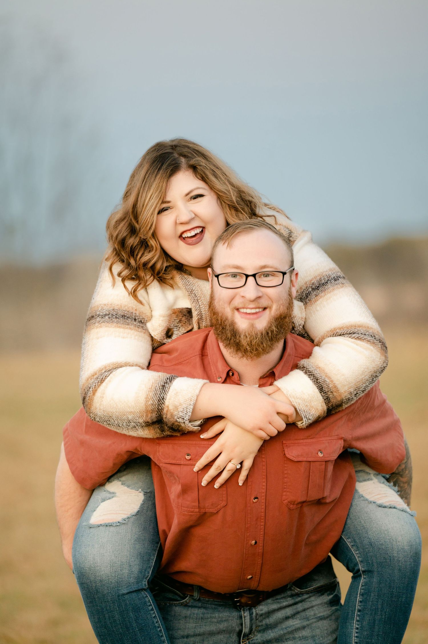 A playful outdoor portrait of a couple laughing and embracing in a grassy field during golden hour. St cloud area engagement photos.