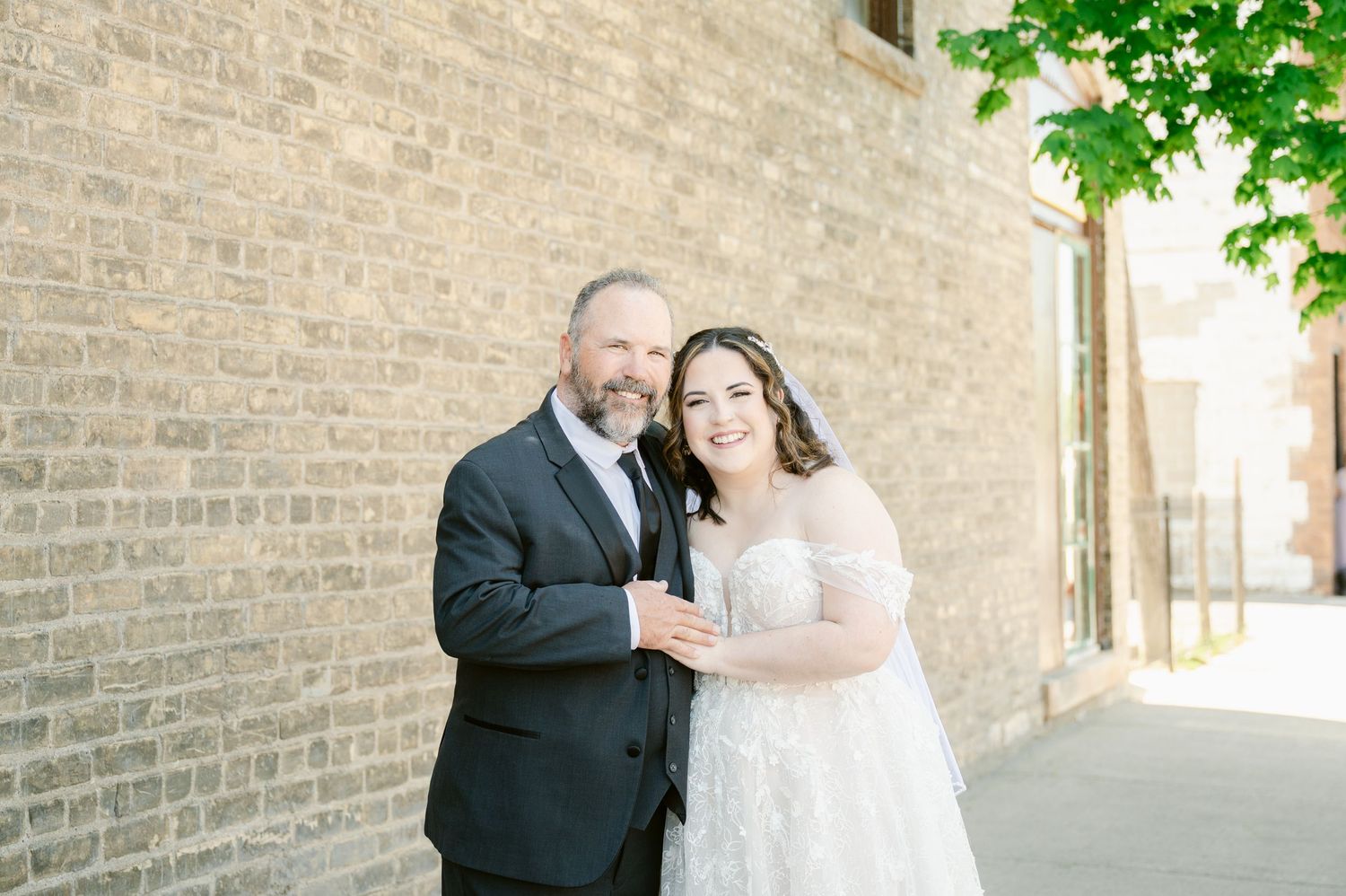 A joyful wedding moment captured against a rustic brick wall backdrop with greenery.