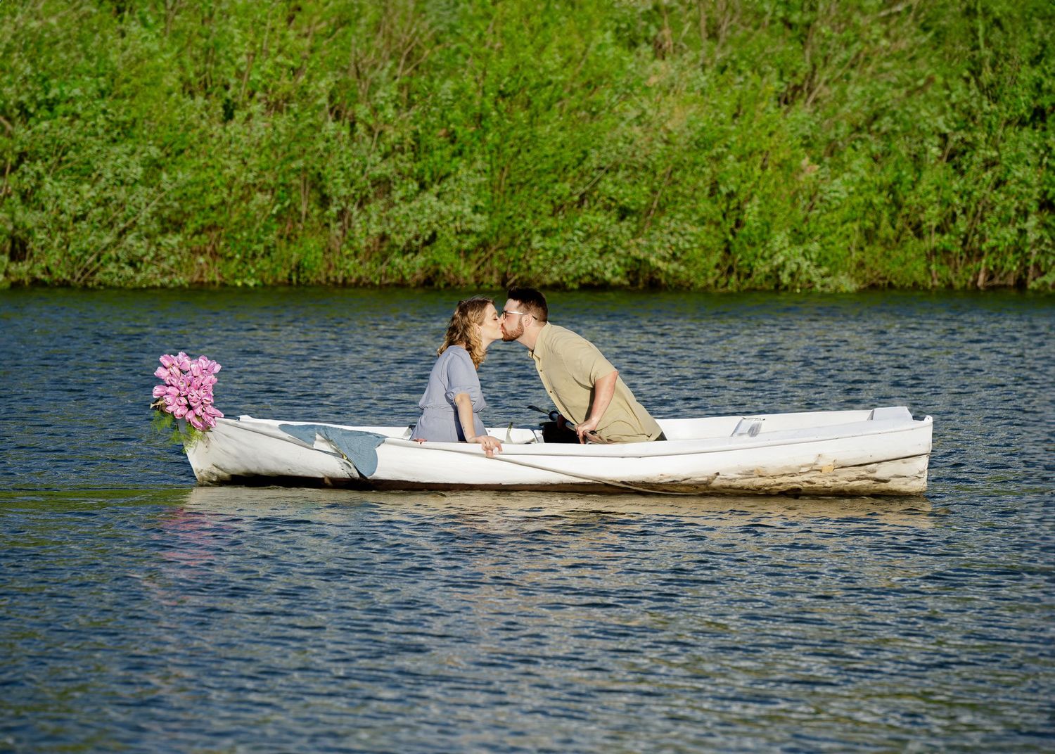 Romantic couple kisses while sitting in white rowboat on peaceful lake.