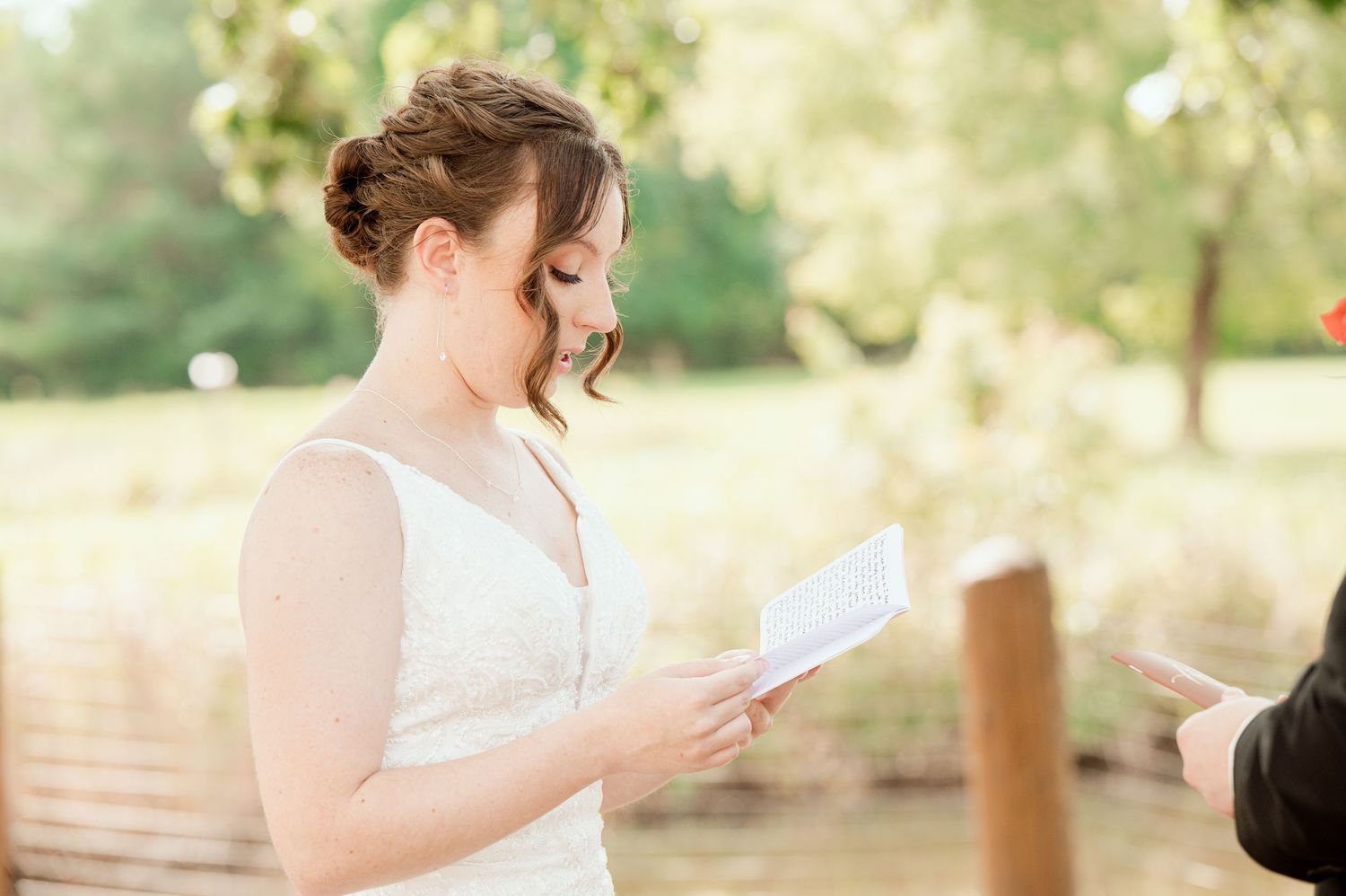 Two people exchange vows during an outdoor wedding ceremony with soft golden sunlight and greenery in the background.