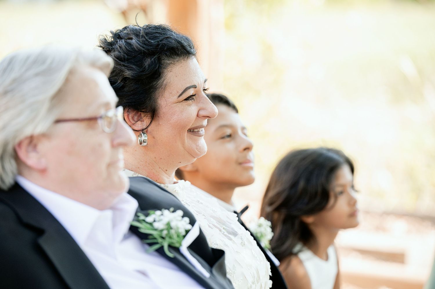 Wedding guests smile joyfully while seated at an outdoor celebration.