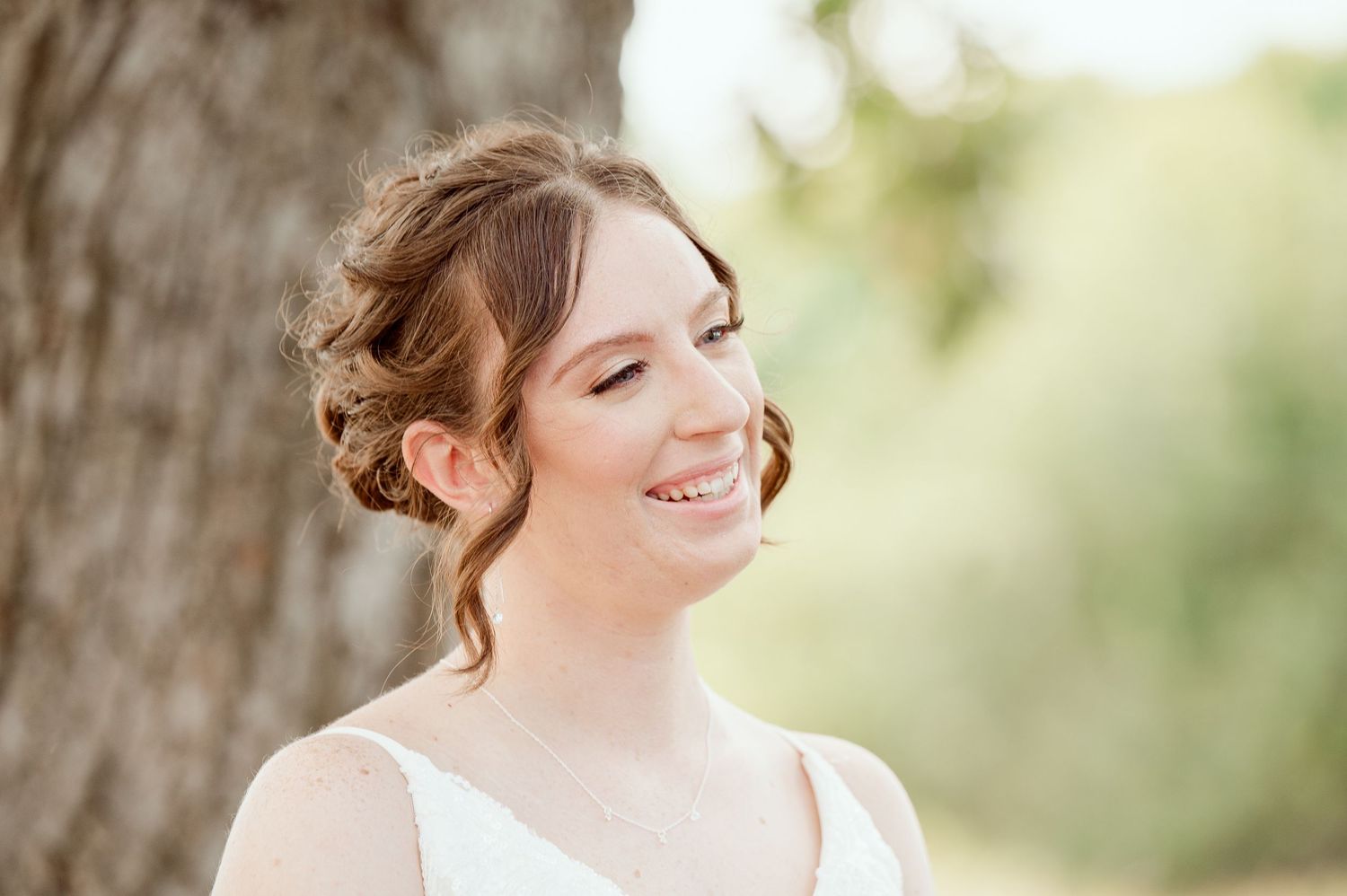The Grands at Mulligans- Wedding Photos: Joyful bride smiles against a soft, natural background with trees and sunlight.