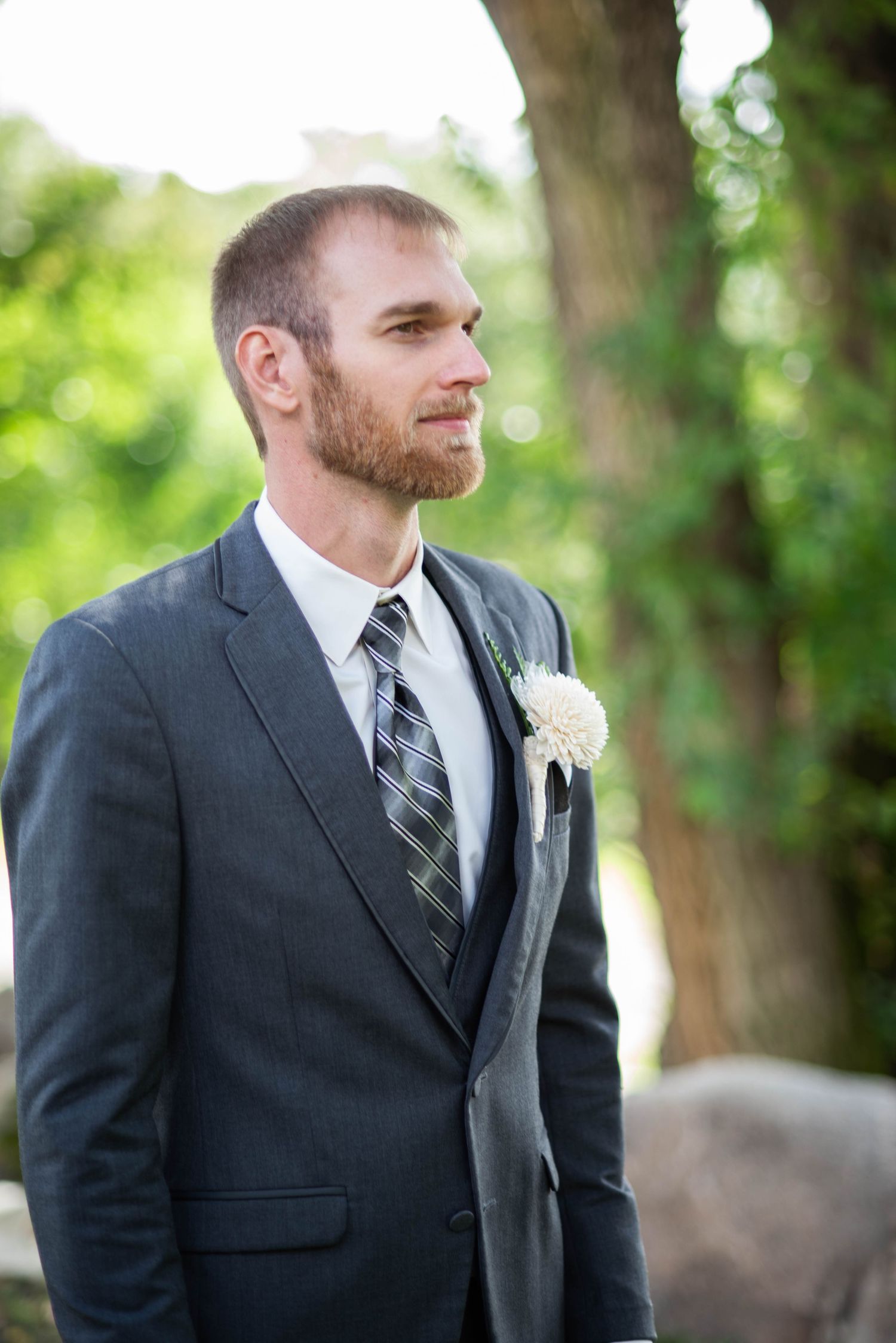 Wedding portrait of groom wearing dark suit and striped tie in outdoor garden setting.