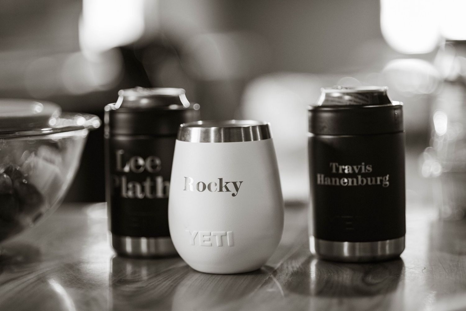 Coffee mugs and cups with names arranged in a row on a counter in black and white photography.