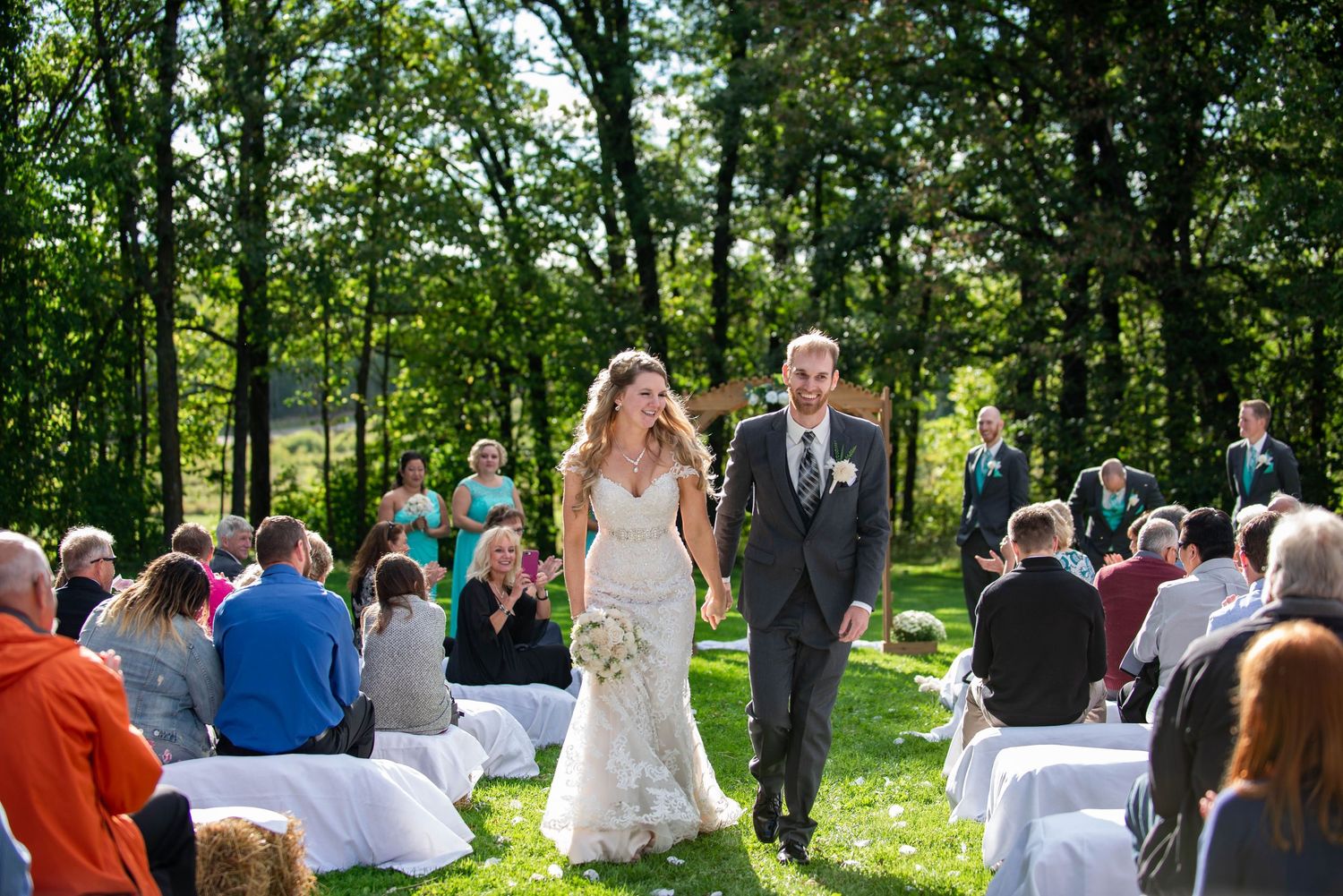 Newlyweds walking down the aisle after their outdoor wedding ceremony surrounded by seated guests. Rum River Barn Milaca Minnesota Weddings