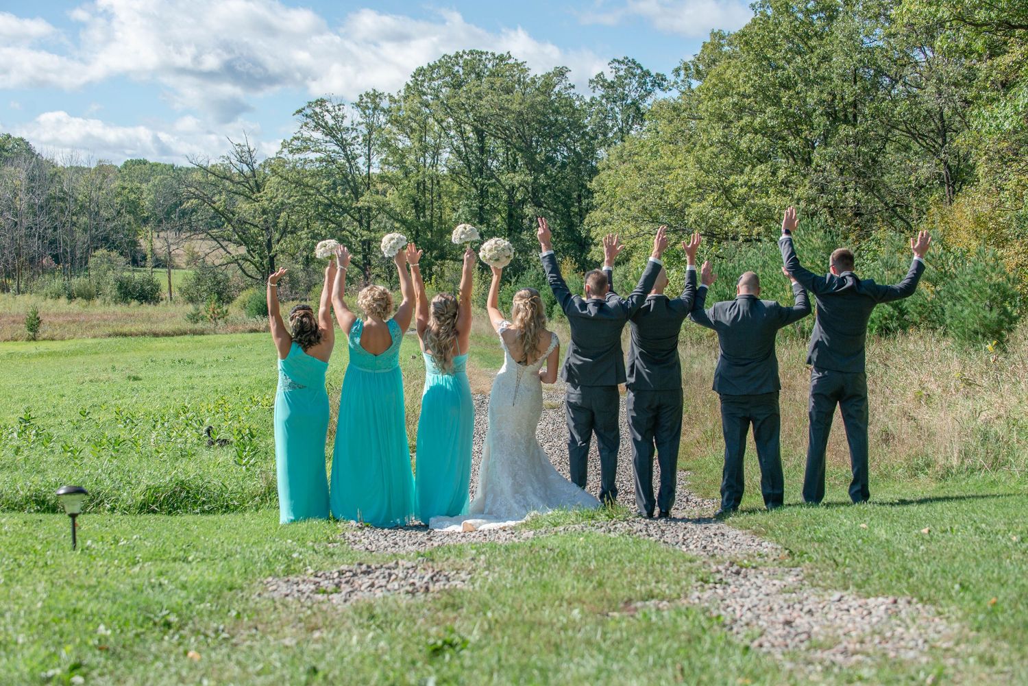 Wedding party posing with raised arms in celebration on a grassy field. Rum River Barn Milaca Minnesota Weddings