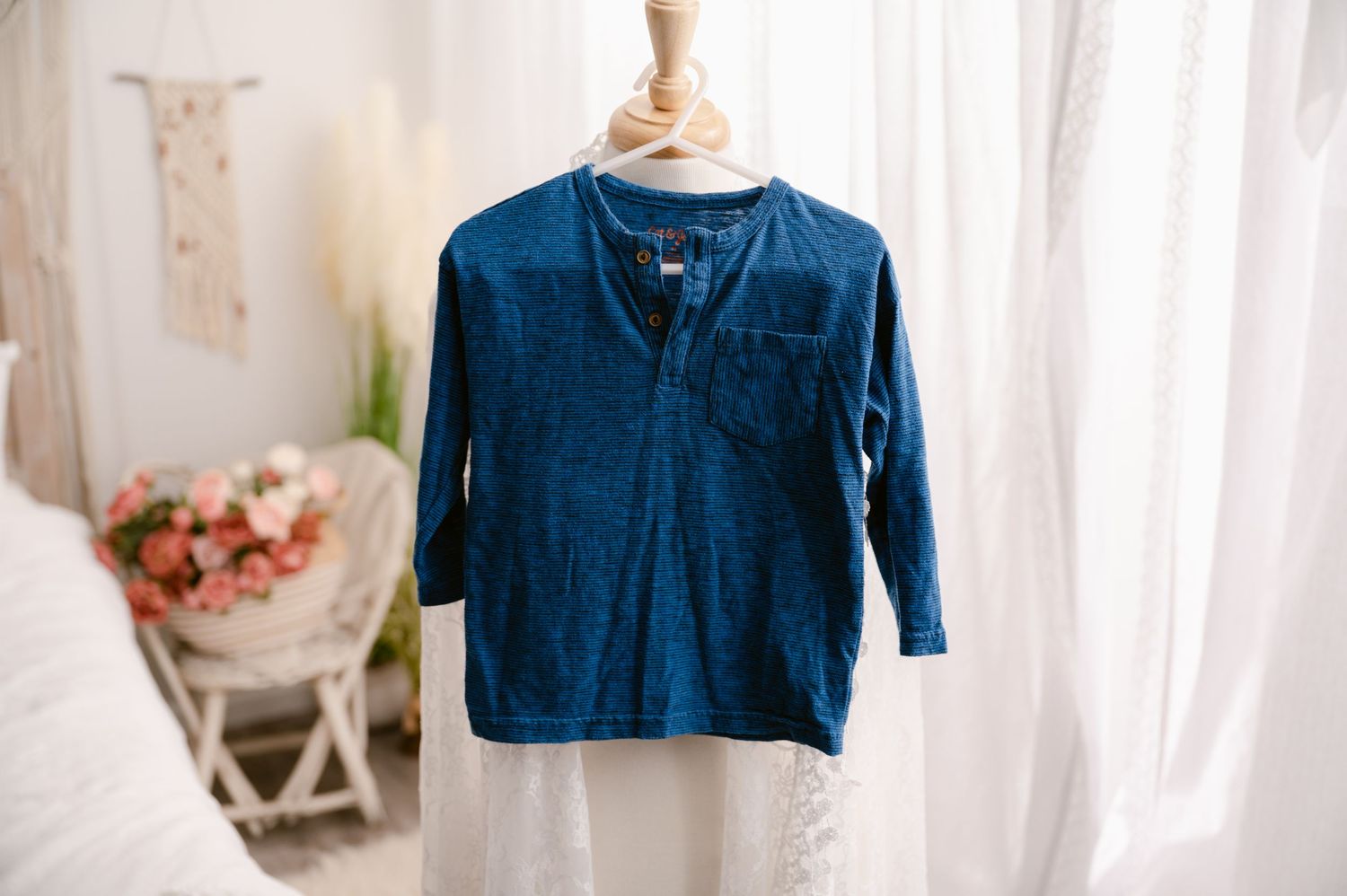 Navy blue quarter-sleeve henley shirt displayed on white mannequin near window and floral arrangement.