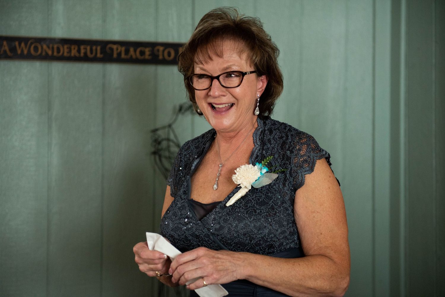 A woman in a navy lace dress holds a white flower against a mint green wall. Rum River Barn Milaca Minnesota Weddings