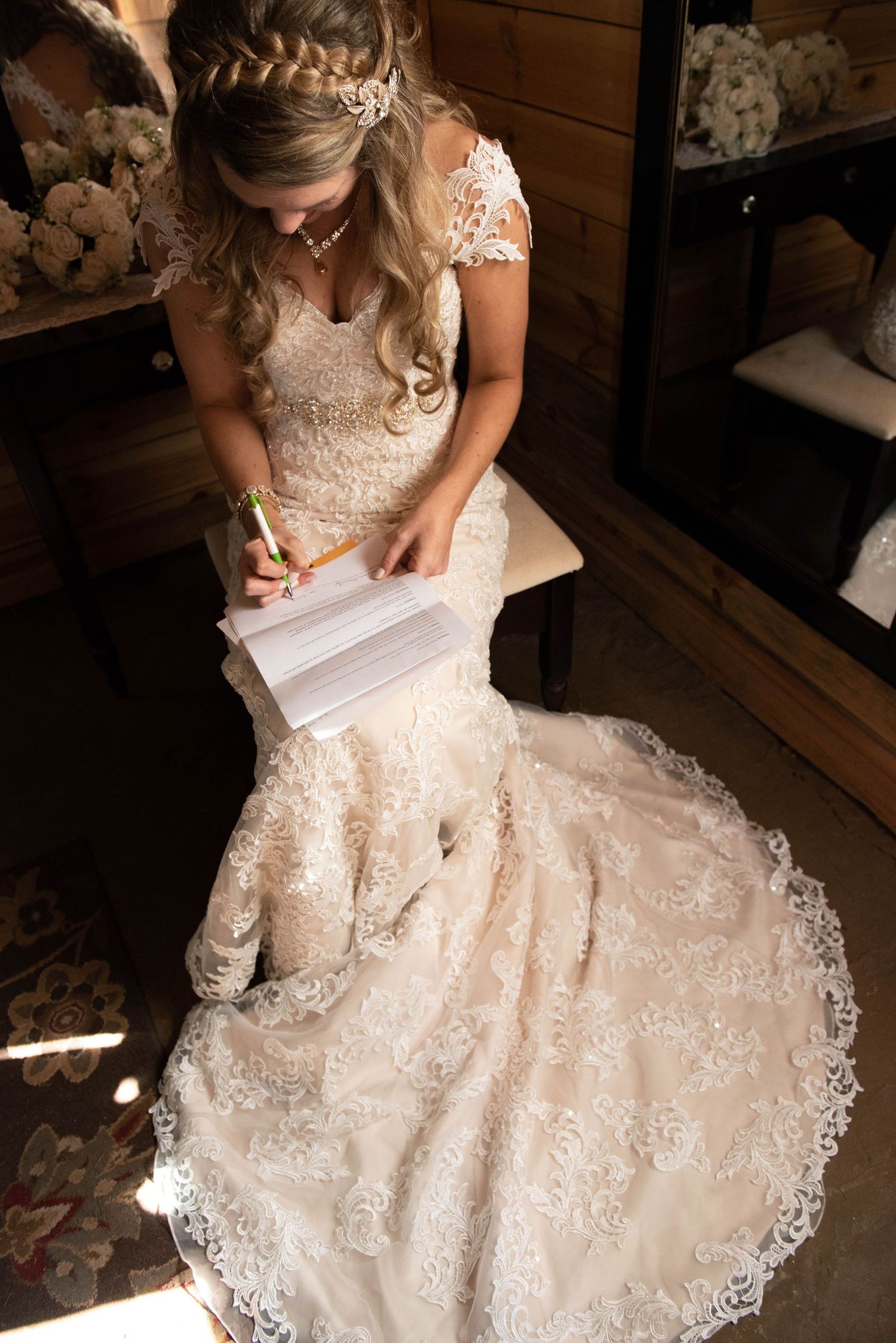 Overhead view of bride in lace gown writing on paper with dress flowing across rustic wooden floor. Rum River Barn Milaca Minnesota Weddings