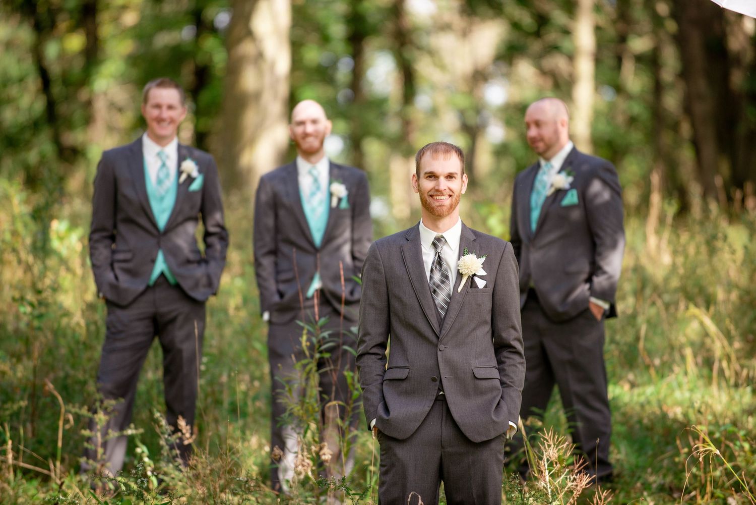 Groomsmen in gray suits with turquoise ties pose casually in a wooded setting. Rum River Barn Milaca Minnesota Weddings
