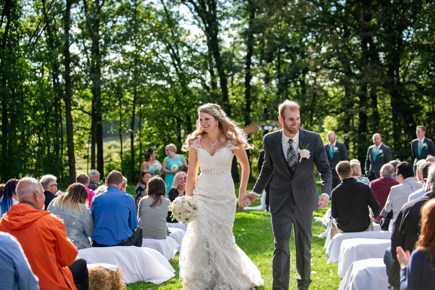 Outdoor wedding guests gather for ceremony among tall trees in a natural park setting. Rum River Barn Milaca Minnesota Weddings
