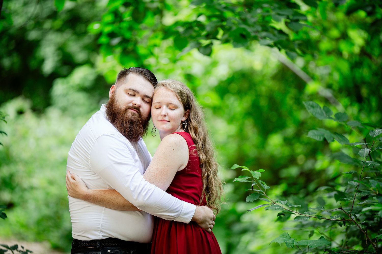 A couple embraces in a romantic outdoor setting surrounded by lush green foliage. St cloud area engagement photos.