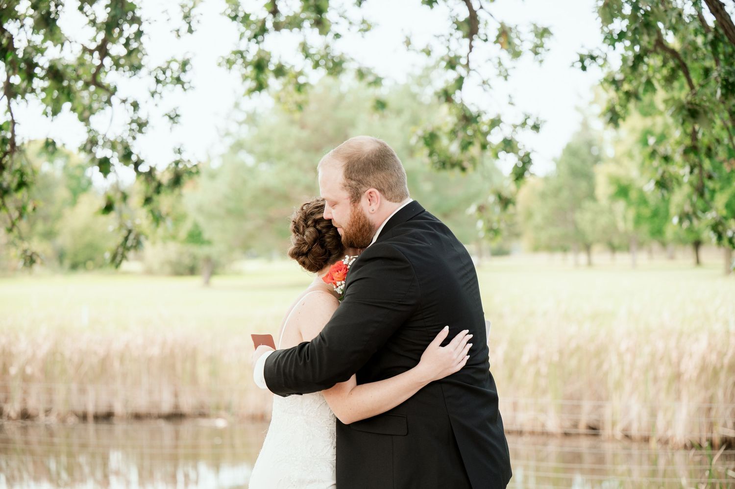 The Grands at Mulligans- Wedding Photos: A couple embraces in a romantic moment among tall grassy fields on an overcast day.