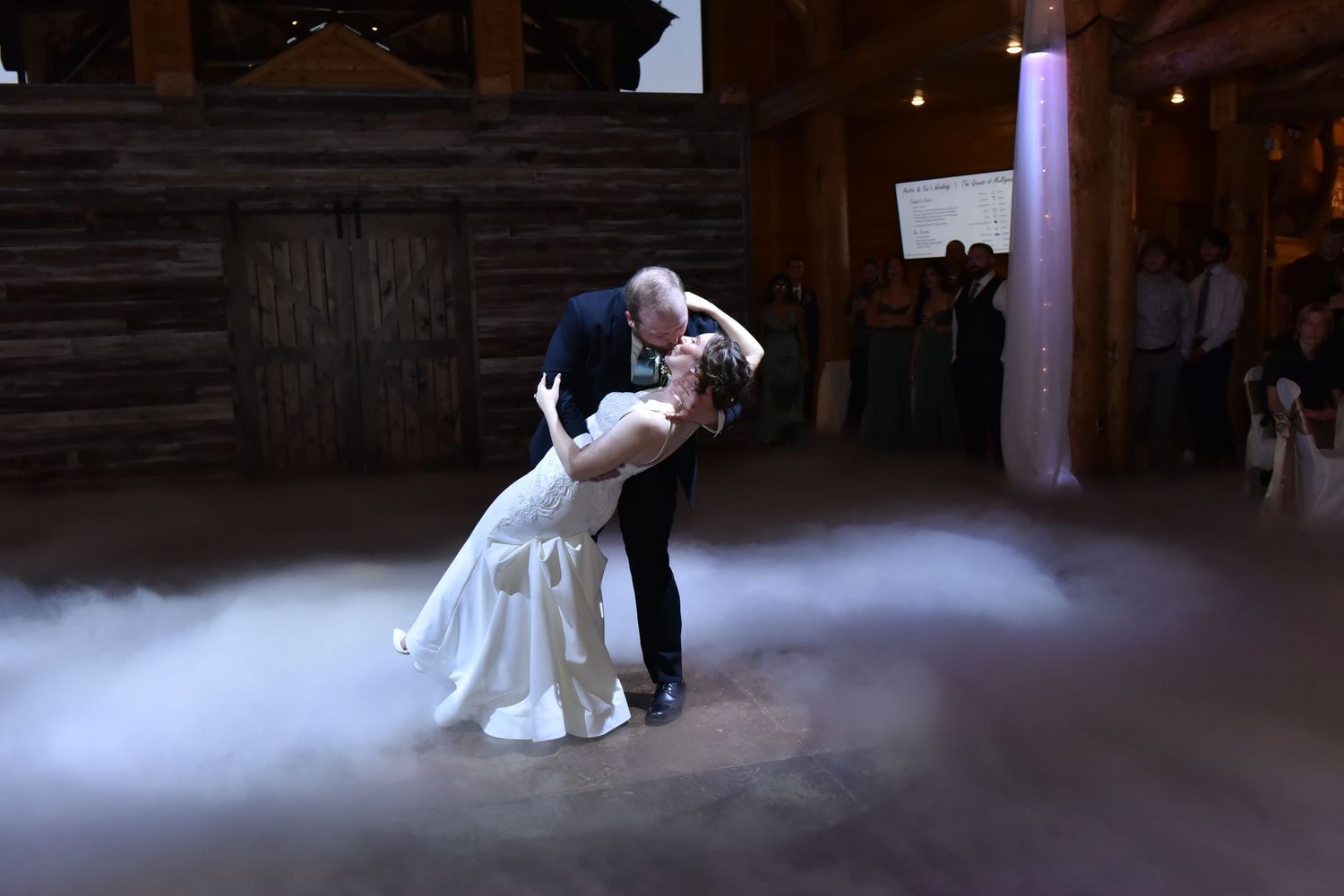 The Grands At Mulligans. A couple shares their first dance in a rustic barn venue with atmospheric fog effects on the dance floor.
