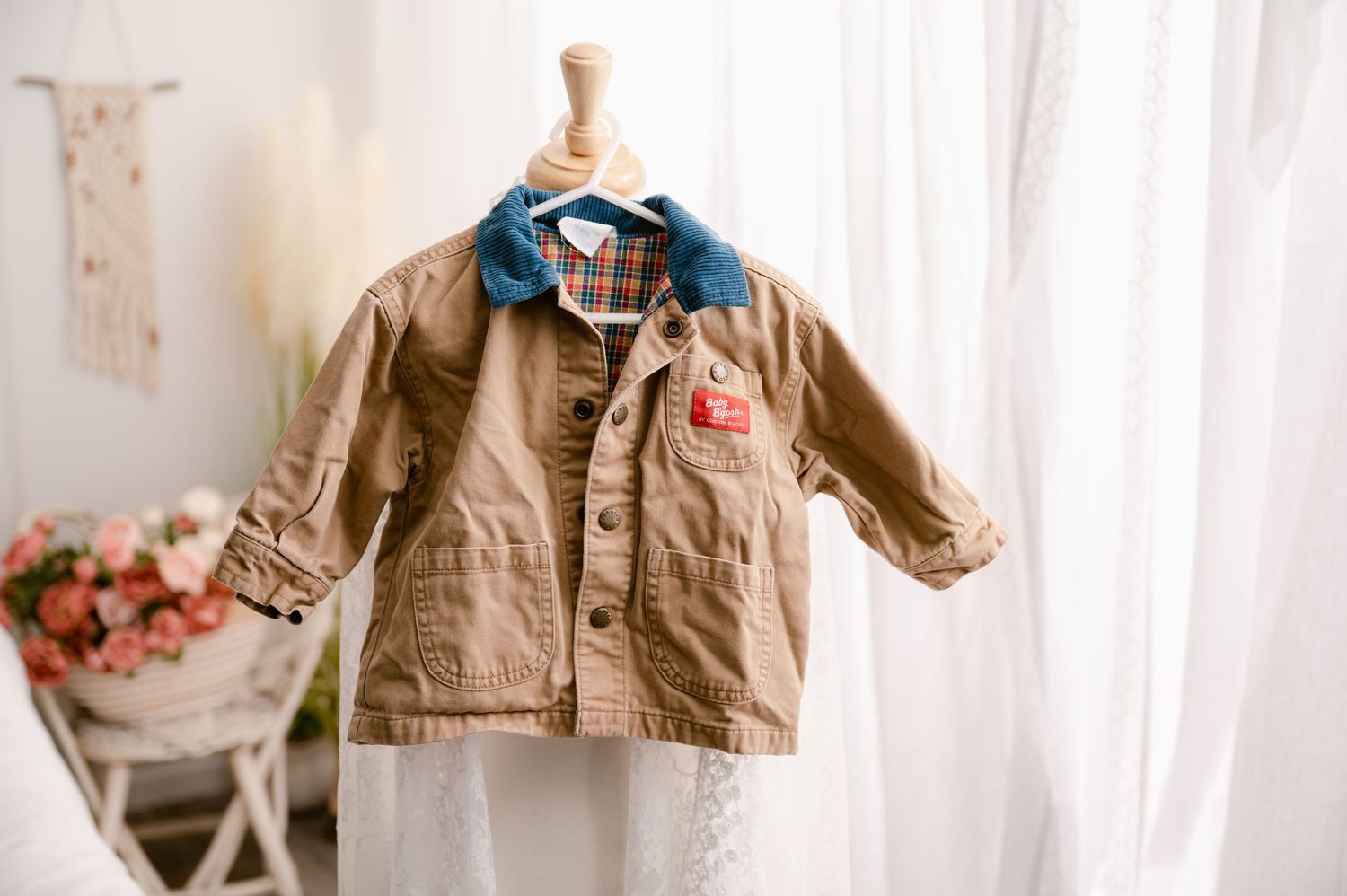 Vintage tan canvas children's jacket with blue collar and red detail hanging on wooden hanger against white background.