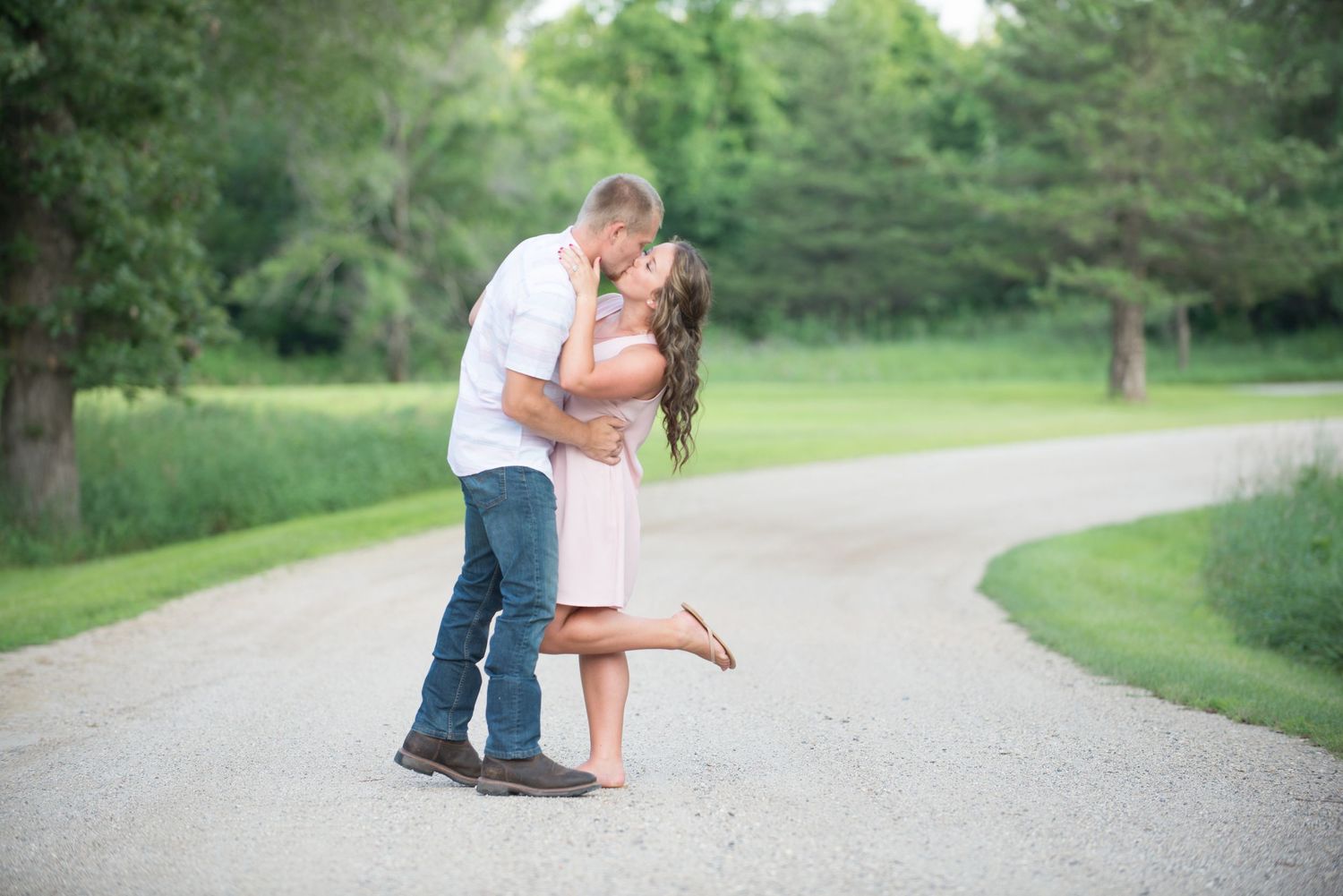 A romantic couple embraces on a curved path during a sunny engagement photoshoot.