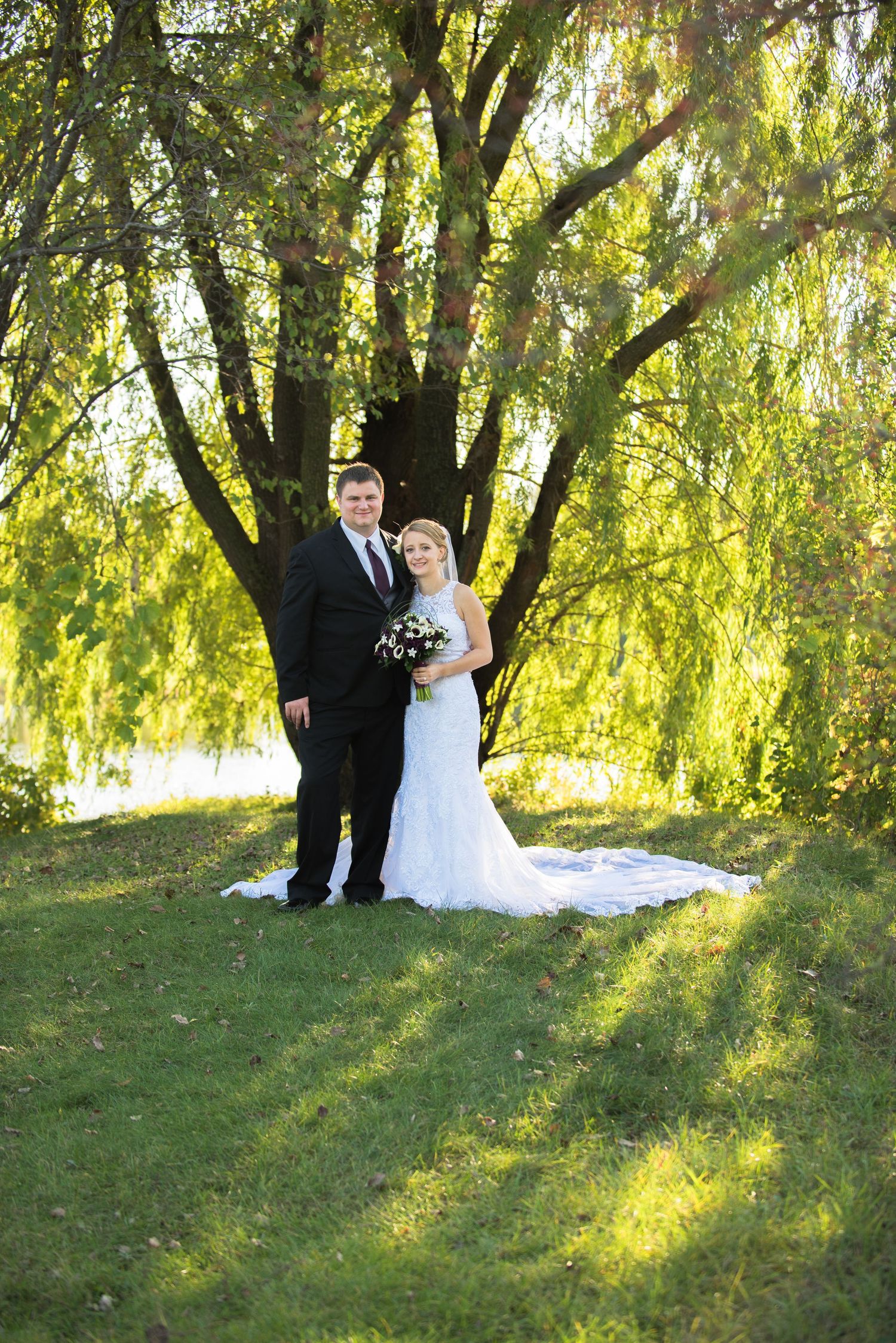 Newlyweds pose for a formal portrait under a majestic weeping willow tree on their wedding day. Andover wedding at Magestic Oaks Golf Club