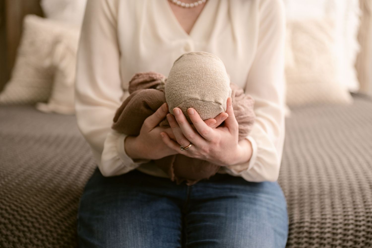Gentle hands cradle a sleeping infant in white sweater on a textured gray blanket.