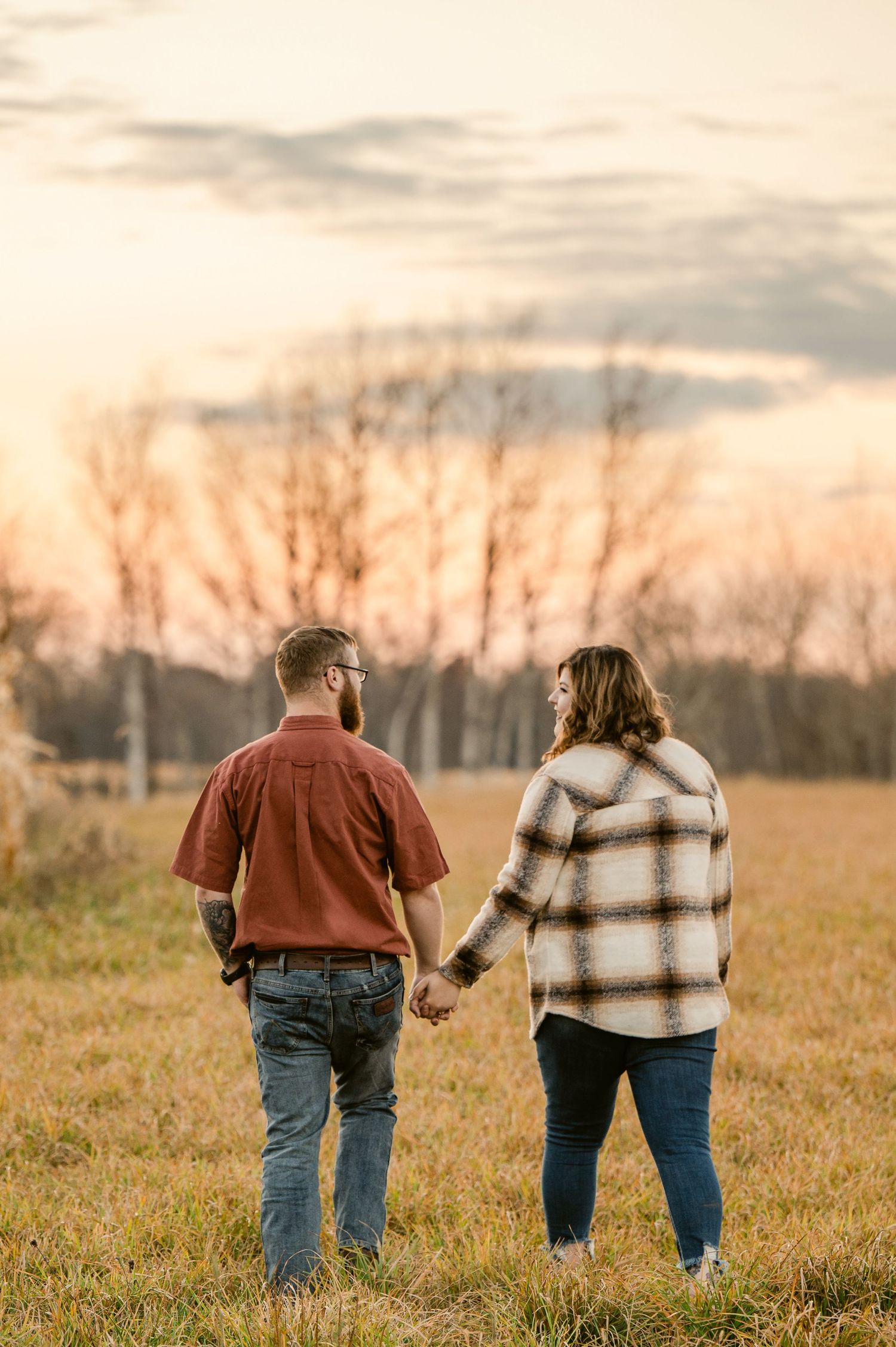 Elderly couple walking hand in hand through a golden field at sunset creating a romantic silhouette.