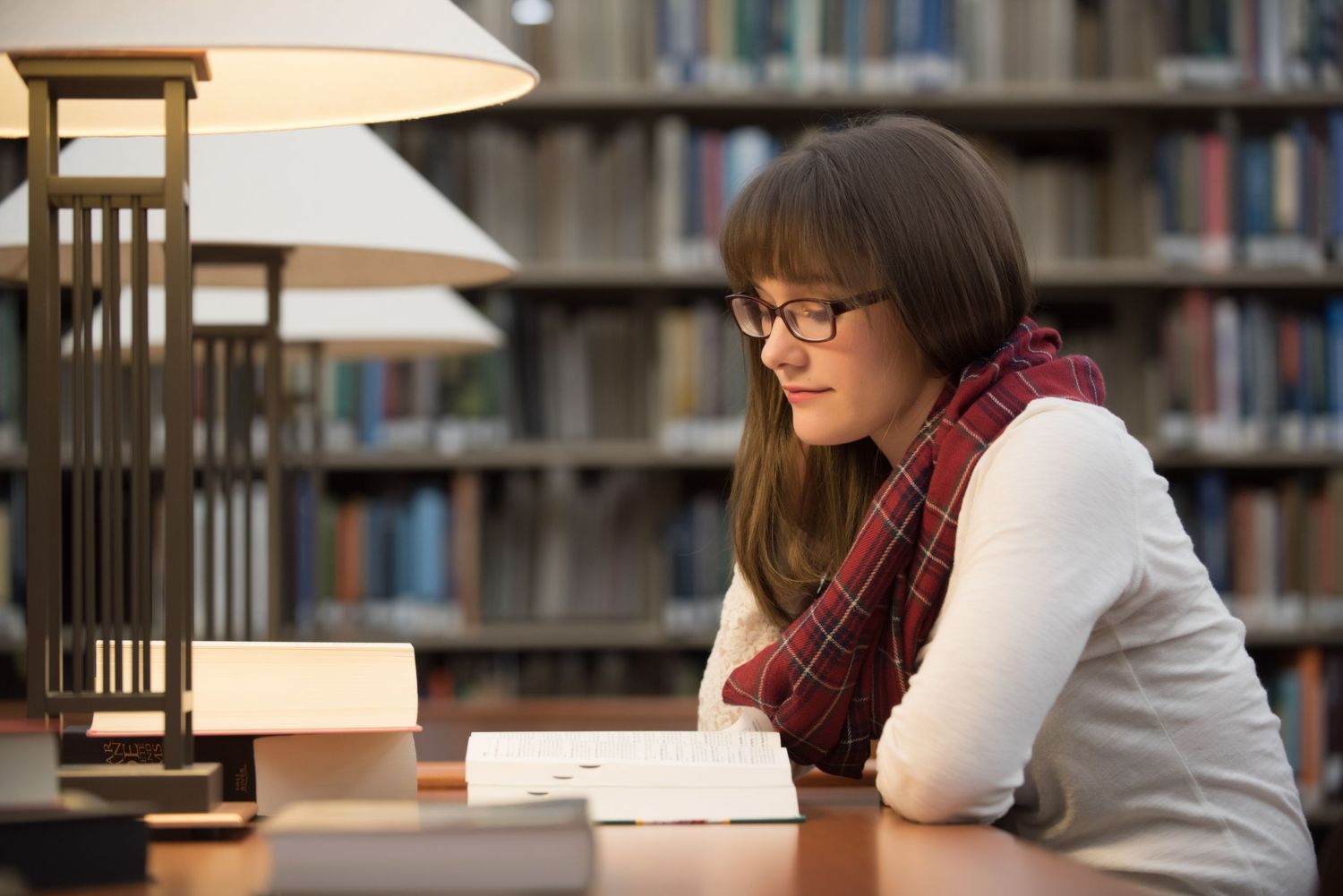 Senior Portrait at St Cloud State College Student studying at wooden desk in library surrounded by bookshelves.