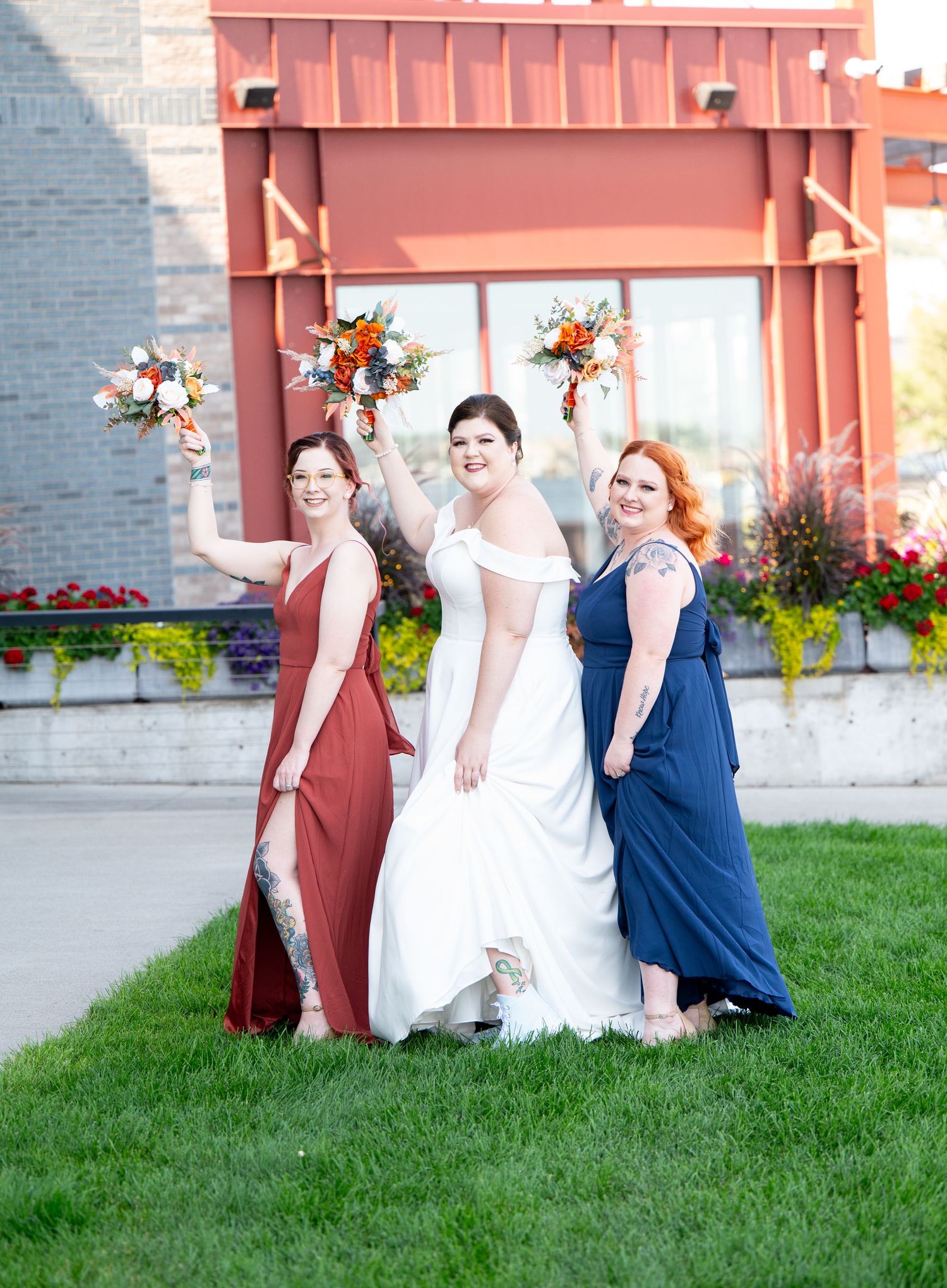 Pier B Duluth Wedding Three wedding party members posing in burgundy, white, and navy dresses against a coral-colored building.