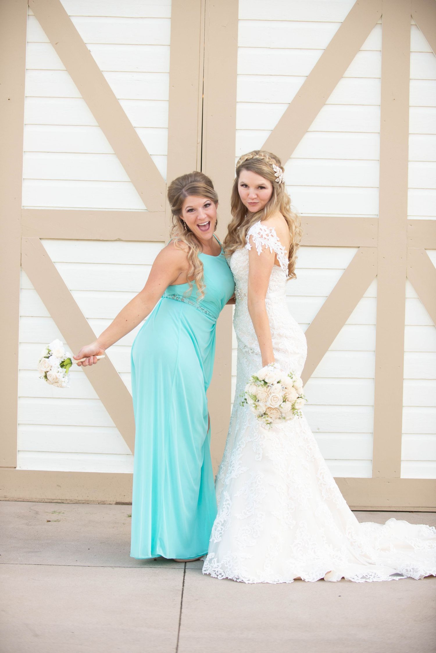 Bride in lace gown and bridesmaid in turquoise dress pose playfully against white barn doors. Milaca Minnesota Weddings