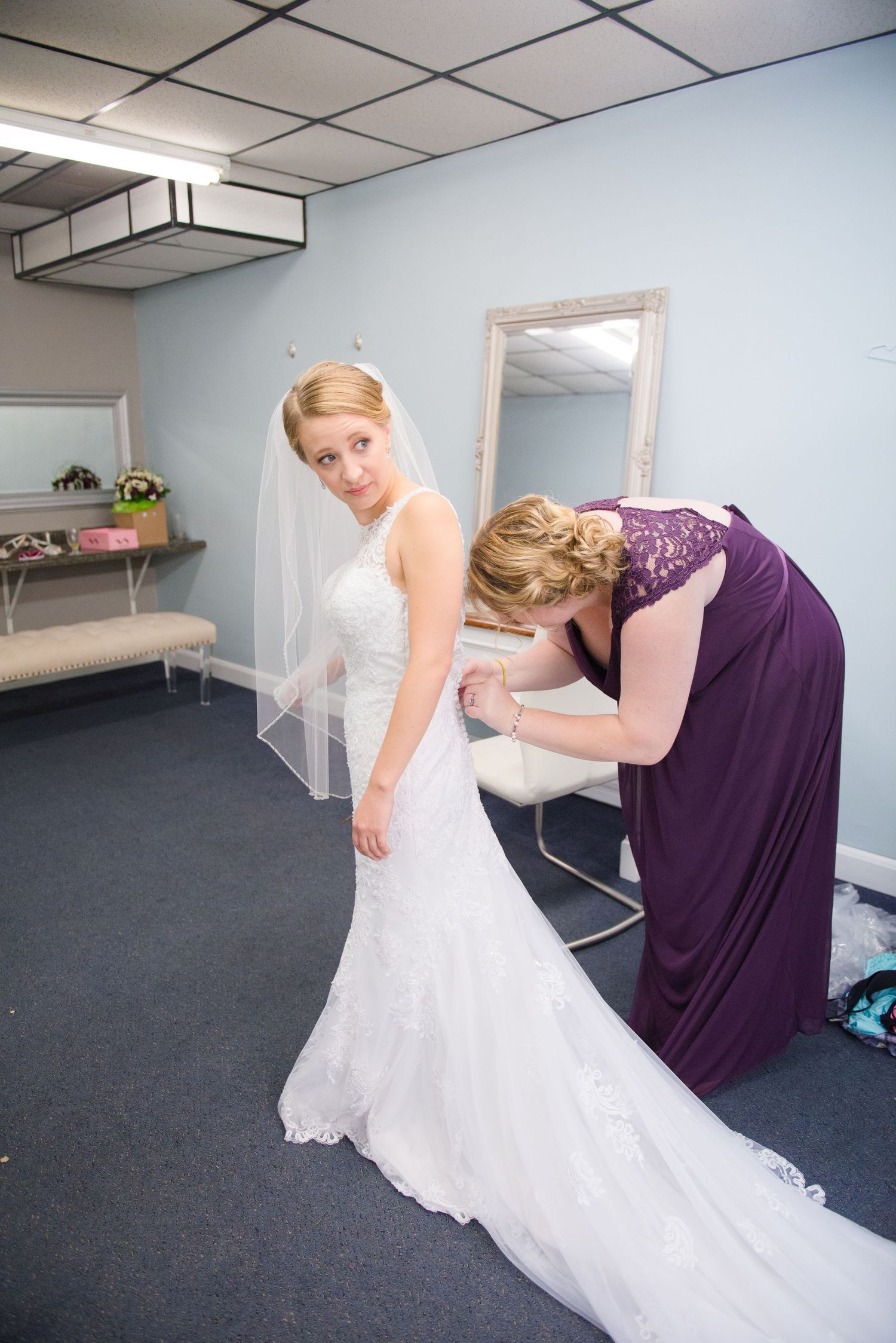 Wedding dress being laced up and adjusted by bridesmaid in purple dress during preparation. Andover wedding at Magestic Oaks Golf Club