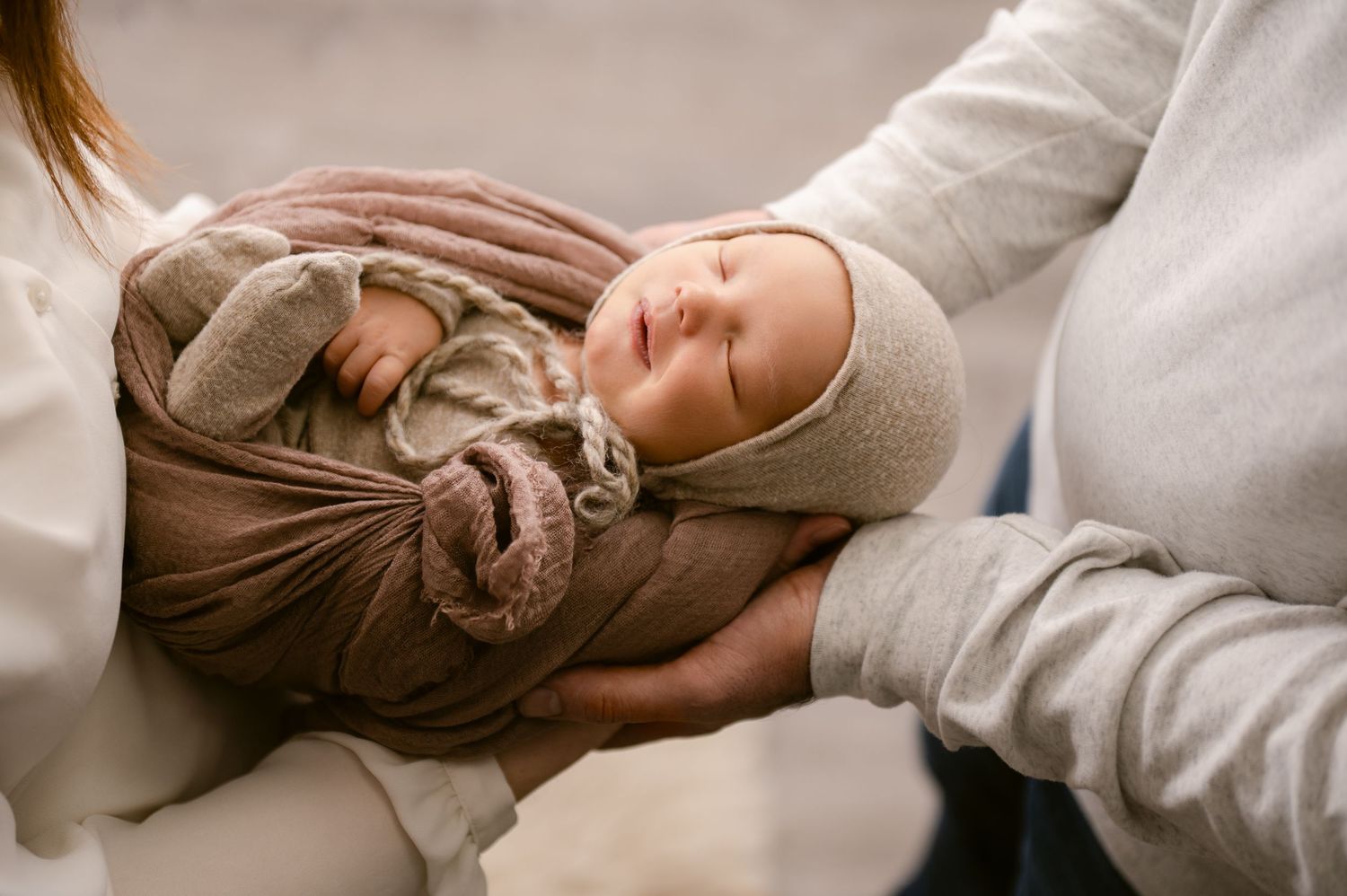 A sleeping newborn baby wrapped in warm brown and beige swaddle blankets rests peacefully on soft bedding.