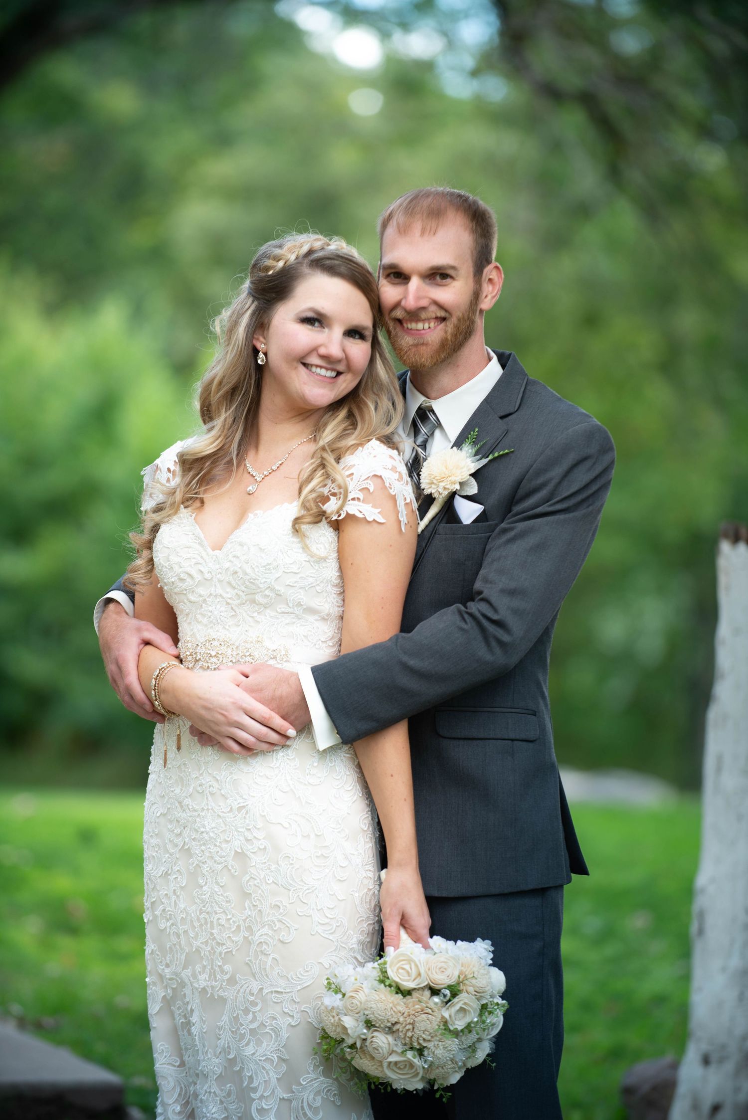 A newlywed couple embraces outdoors in a garden setting with white floral bouquet and formal wedding attire. Rum River Barn Milaca Minnesota