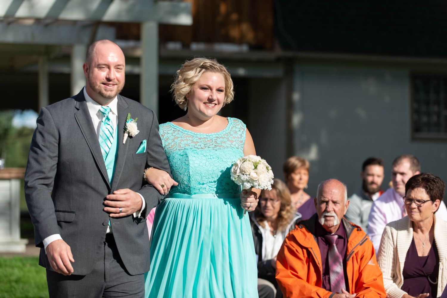 Wedding processional moment outdoors with attendees in turquoise and formal attire. Rum River Barn Milaca Minnesota Weddings