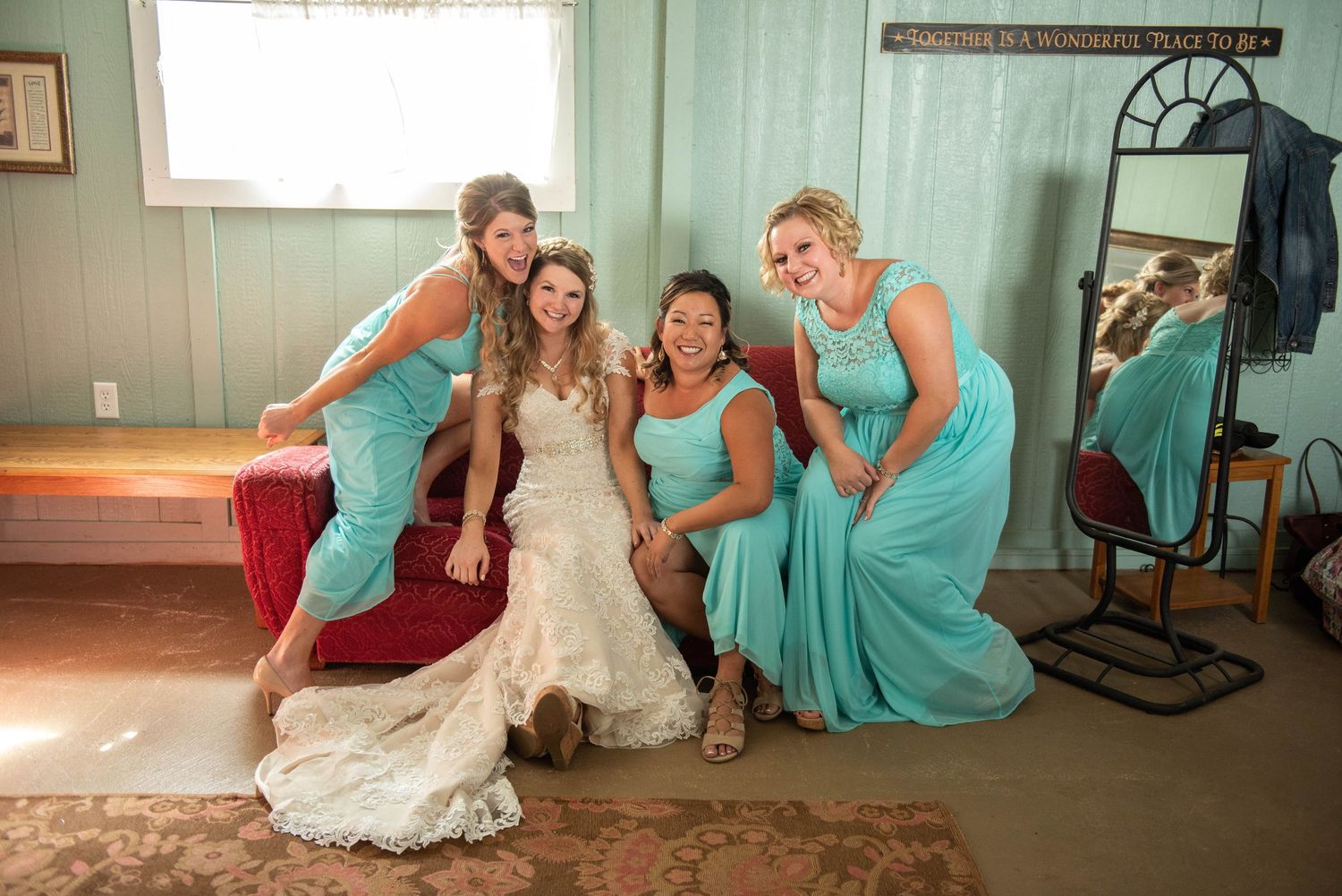 Wedding party poses playfully in turquoise dresses inside rustic room with wooden walls. Rum River Barn Milaca Minnesota Weddings