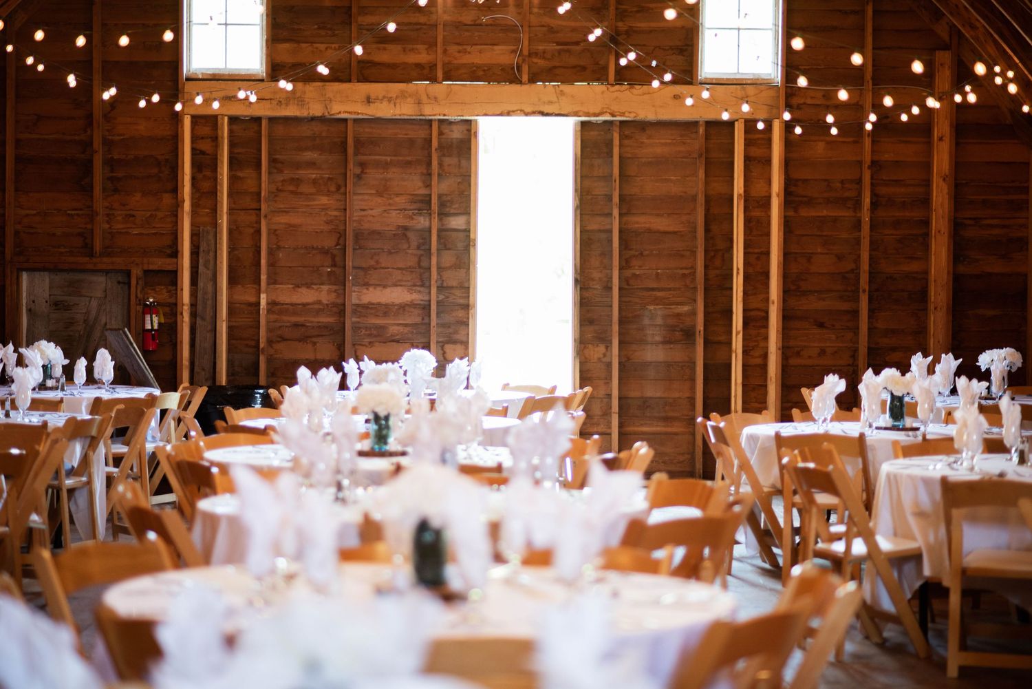 Rustic barn wedding reception venue with string lights and elegantly set dining tables.