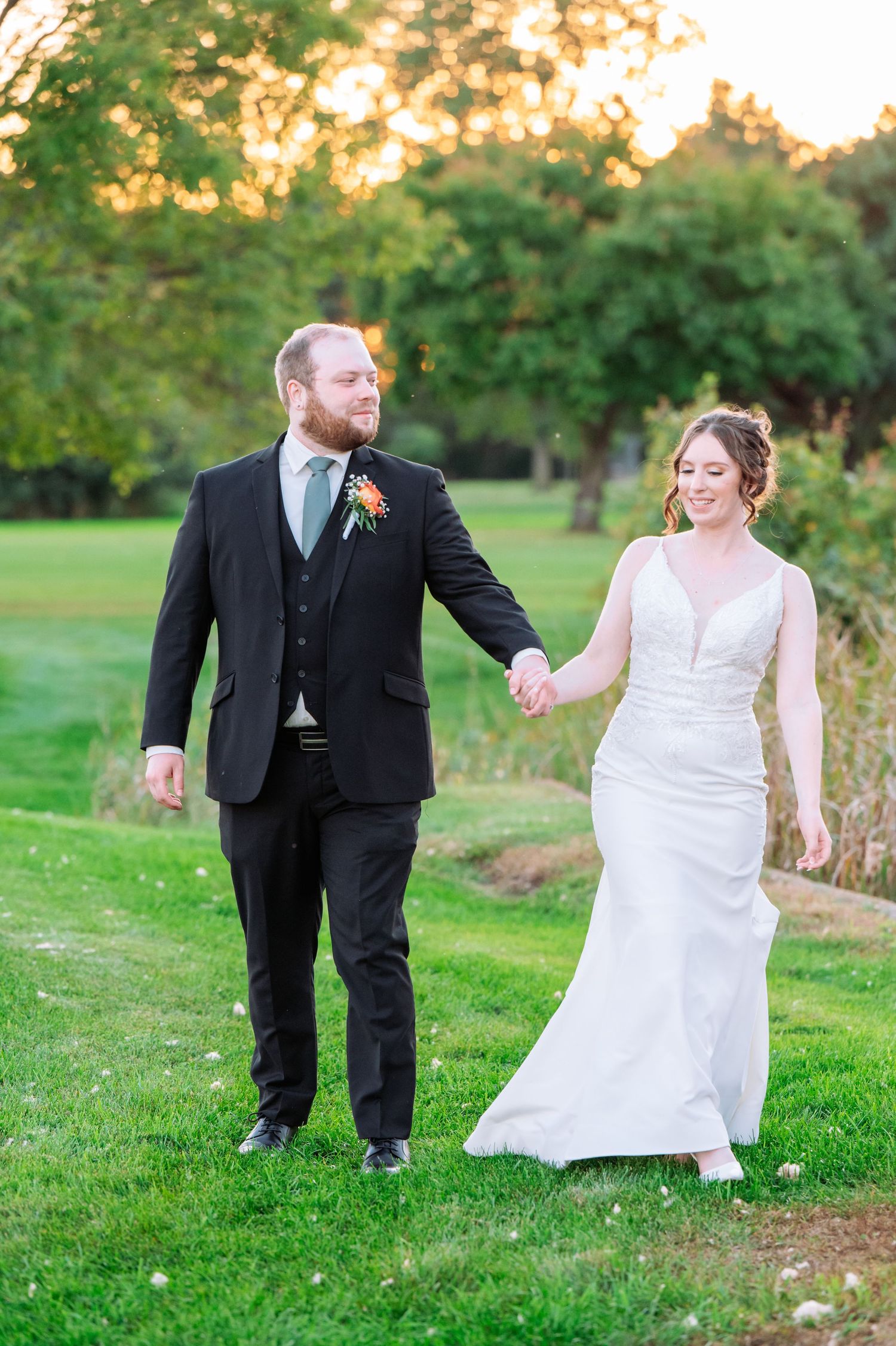 A couple walks hand in hand through a sunlit garden during golden hour.