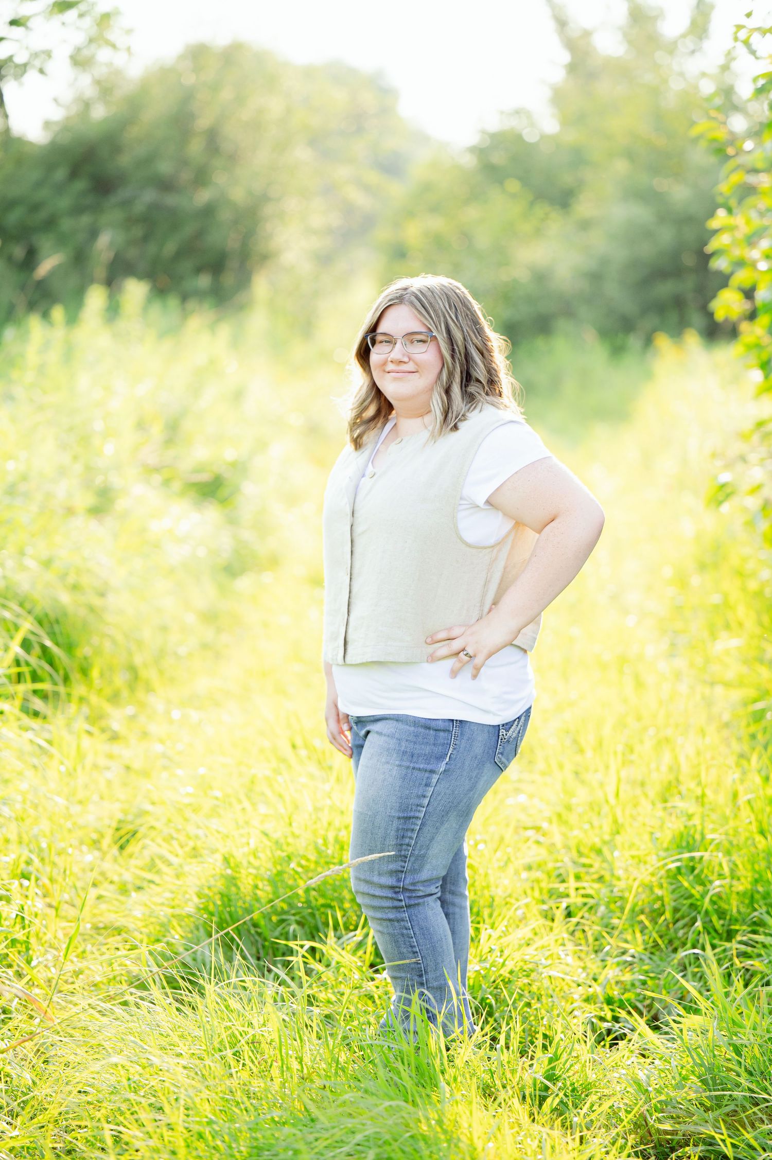 Senior Portrait in Foreston MN in light top and jeans stands in sunny meadow with tall golden grass.