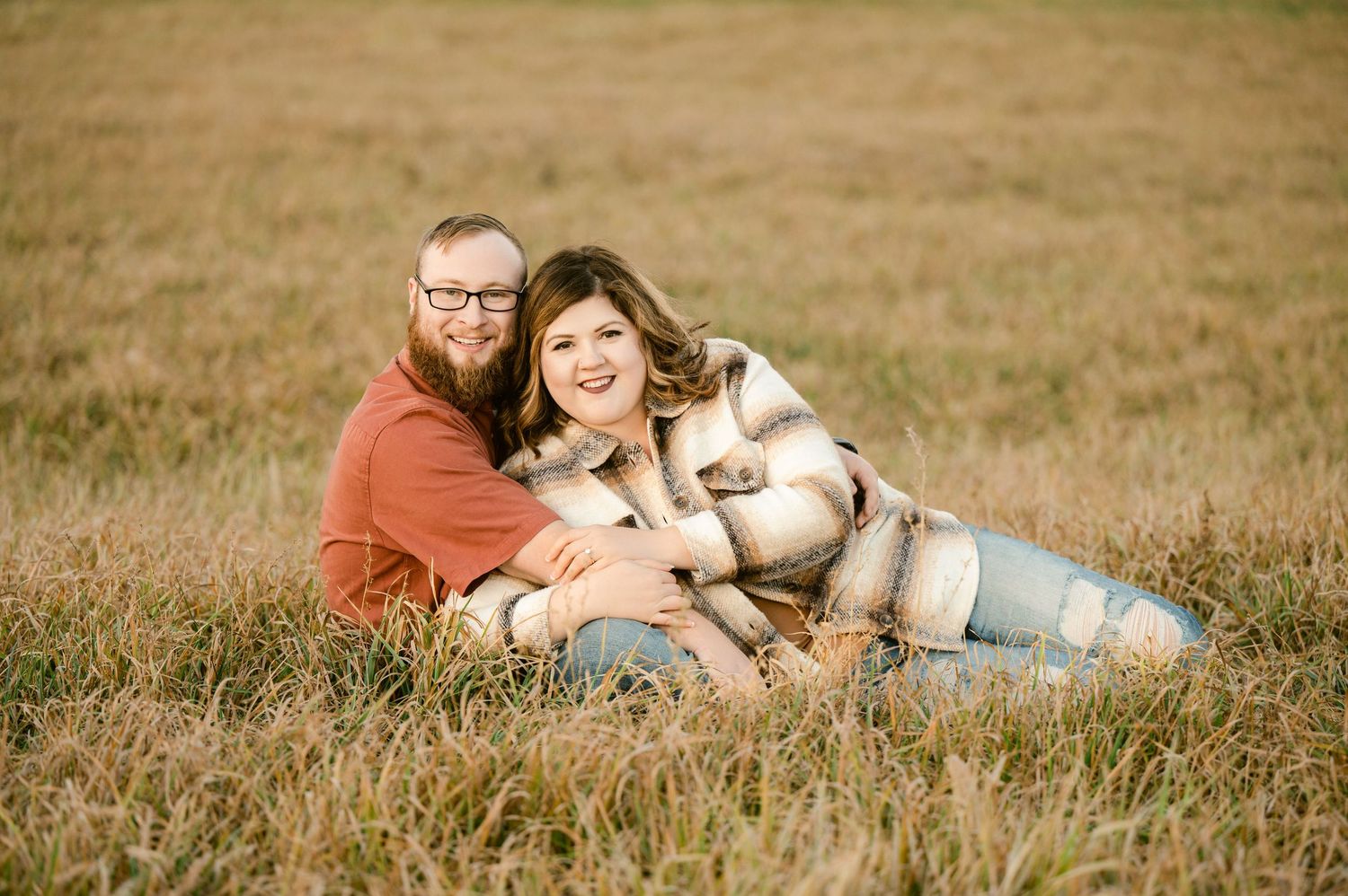 A happy couple relaxes with their dog in a rustic meadow on a sunny afternoon.