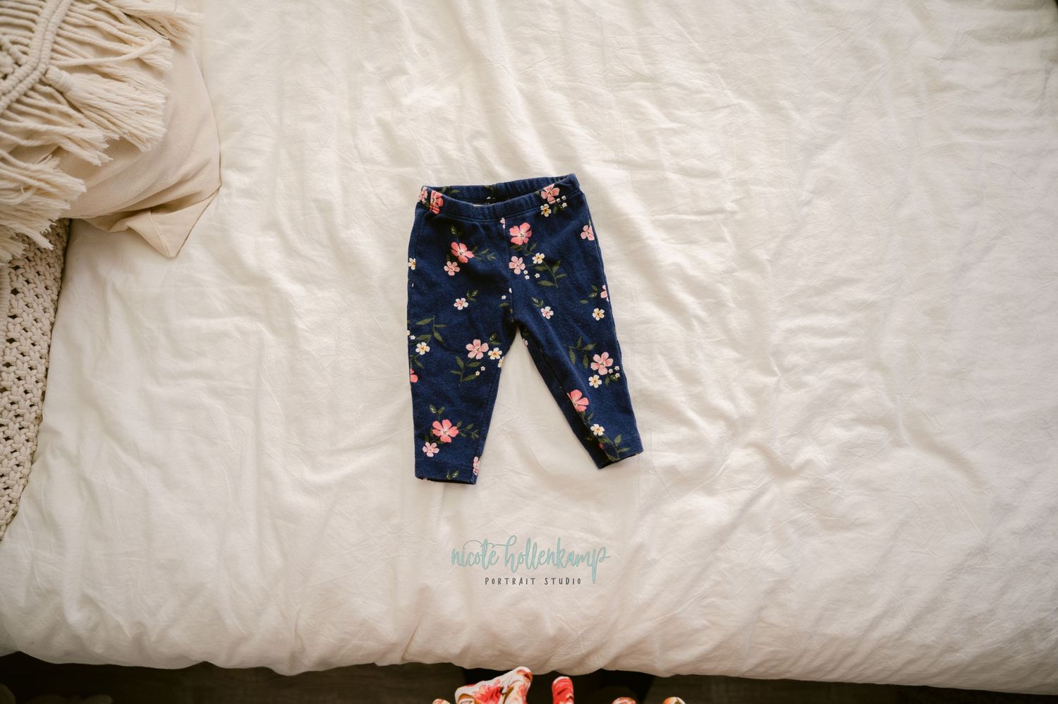 Navy blue baby leggings with pink floral pattern laid out on white bedding.