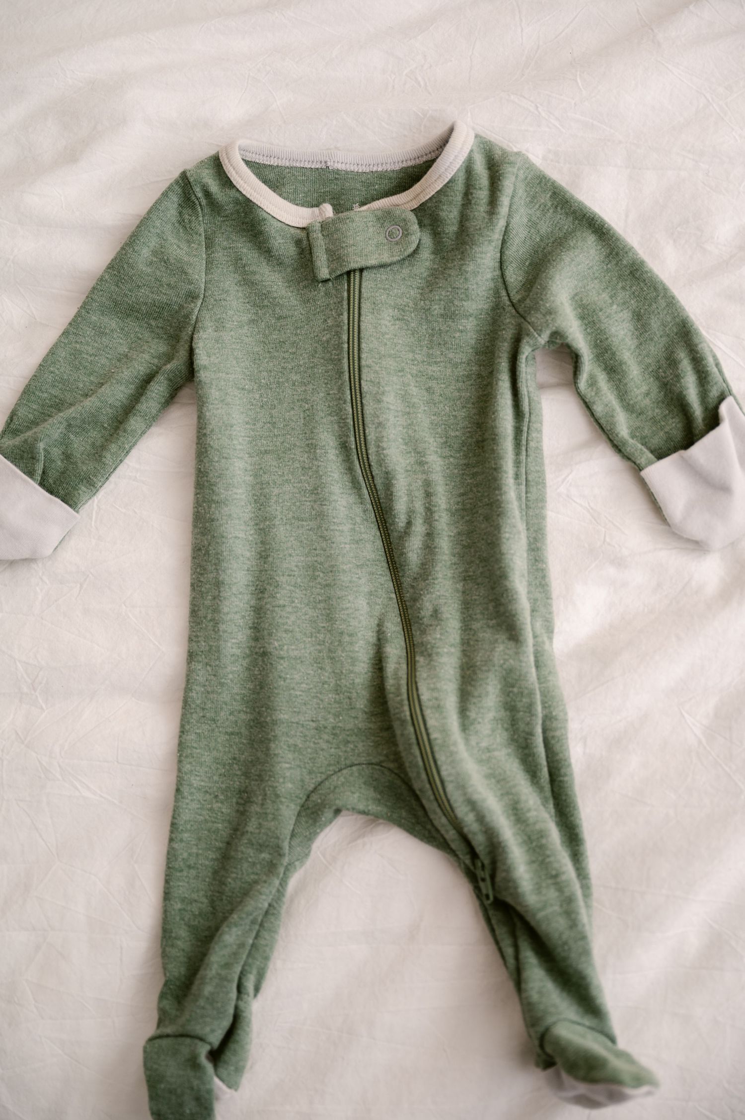 A sage green baby sleeper with long sleeves and footies laid flat on a white surface.
