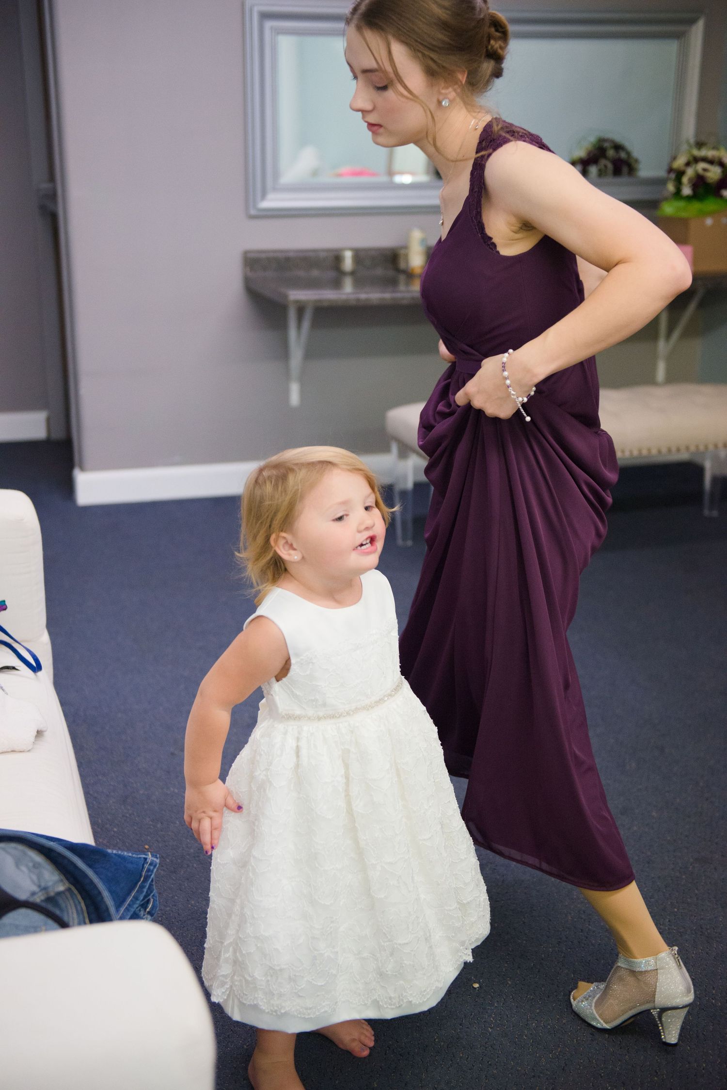 A bridesmaid in purple and flower girl in white share a joyful moment during wedding preparations. Andover wedding at Magestic Oaks Golf Clu