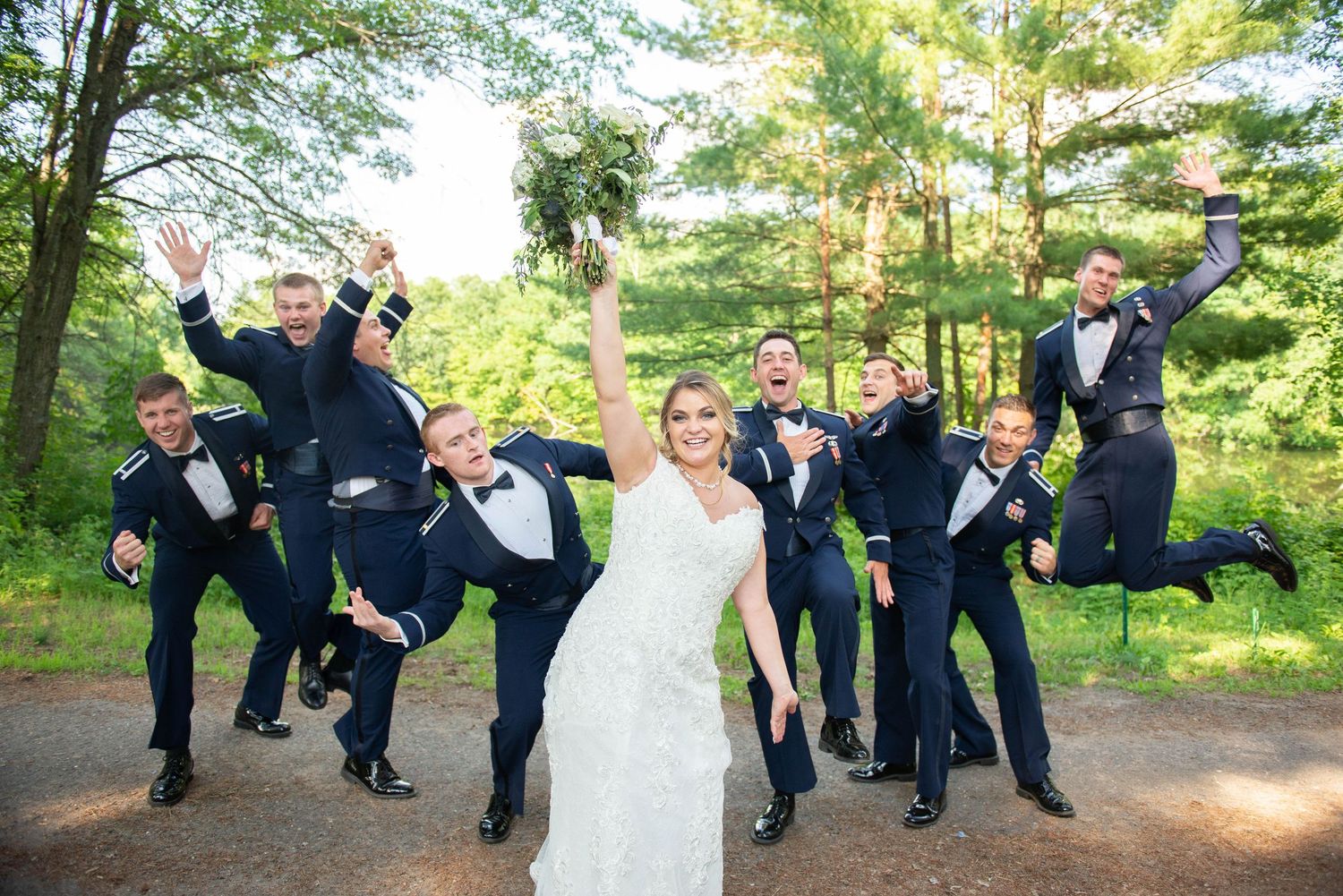 Groomsmen in navy suits perform synchronized jumping poses outdoors in a forest setting. Zimmerman MN Weddings
